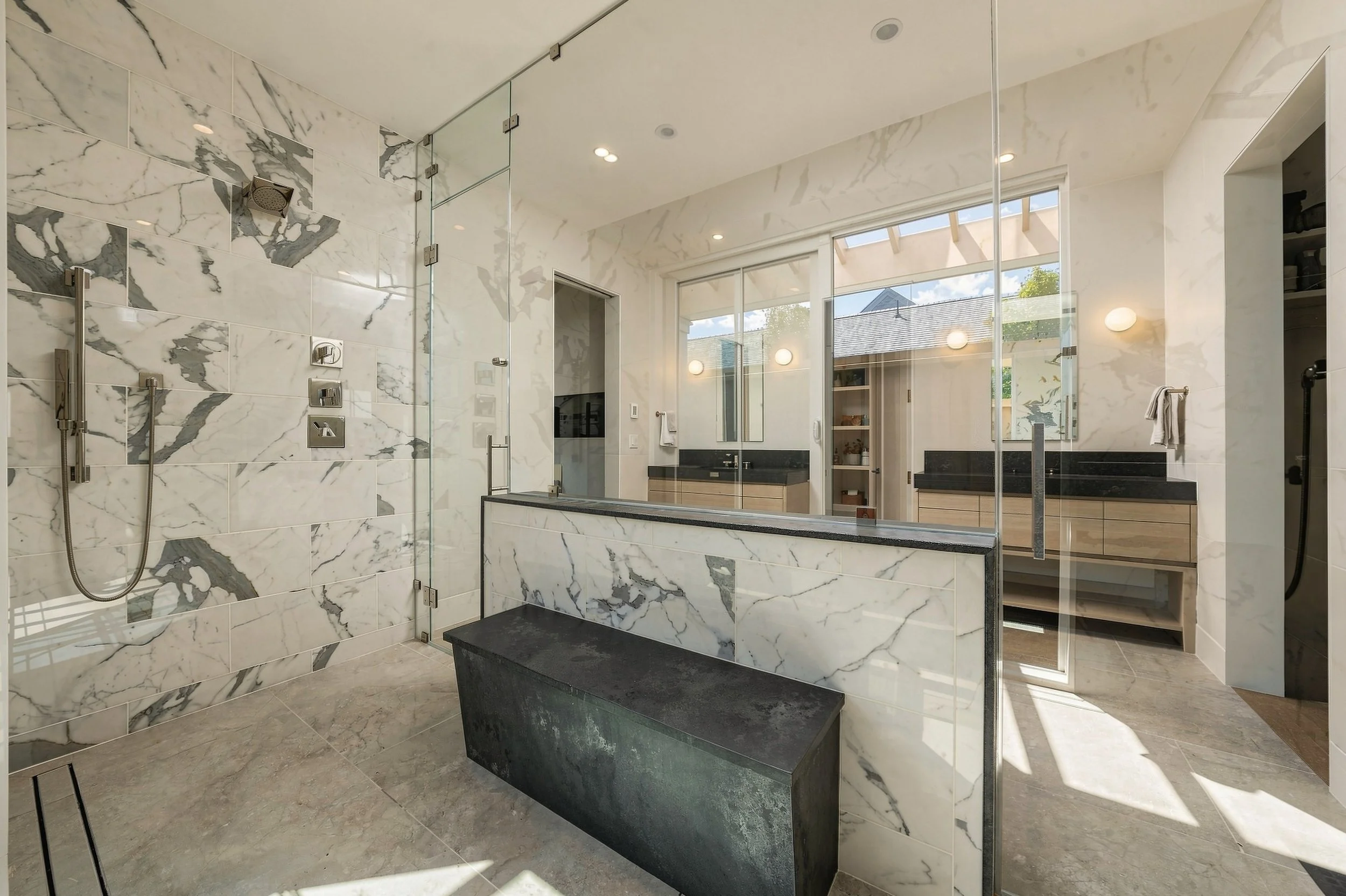 Marble-clad primary shower with a glass enclosure, built-in bench and adjoining double vanity