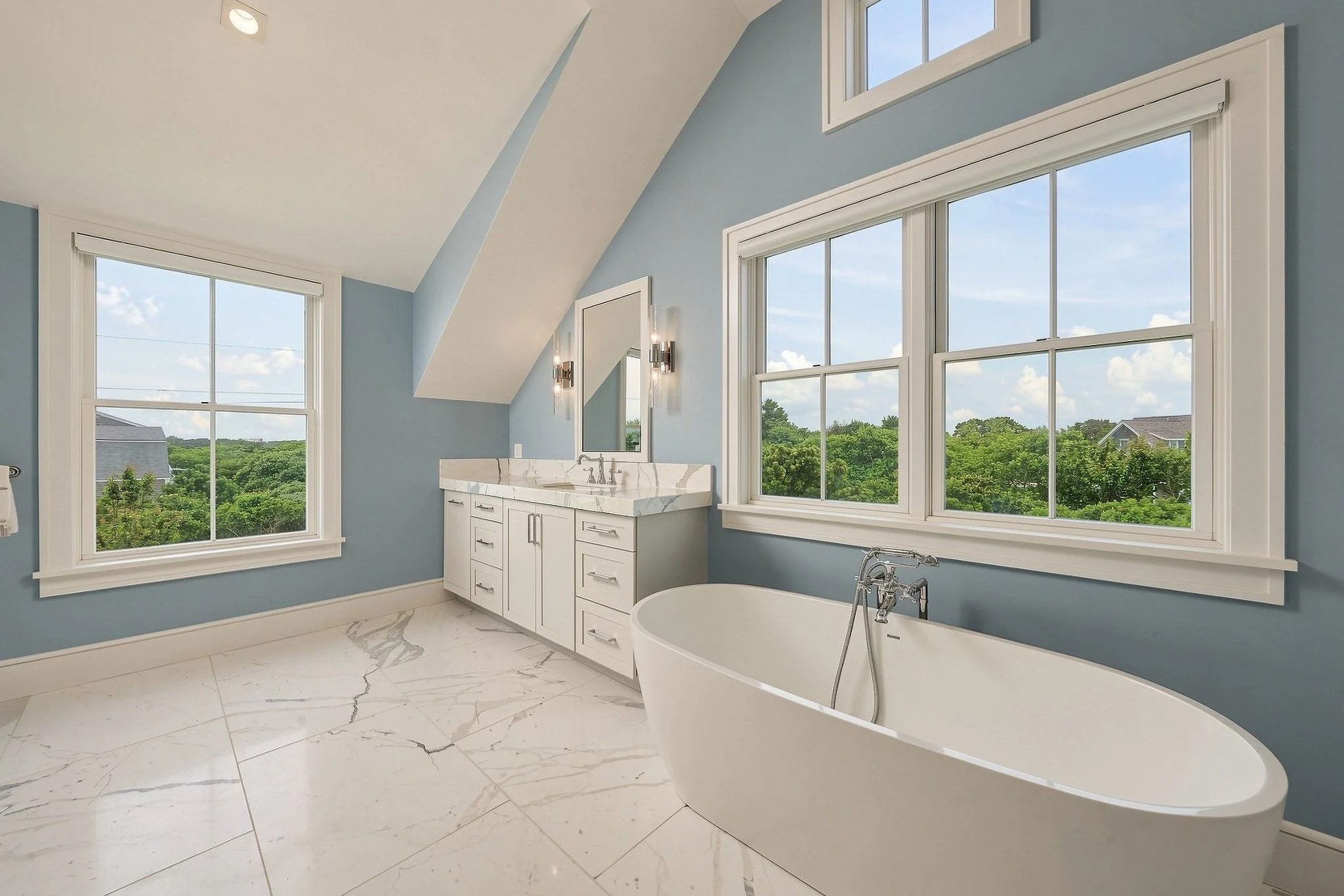 Blue-and-white bathroom with a freestanding tub, double vanity and windows overlooking greenery