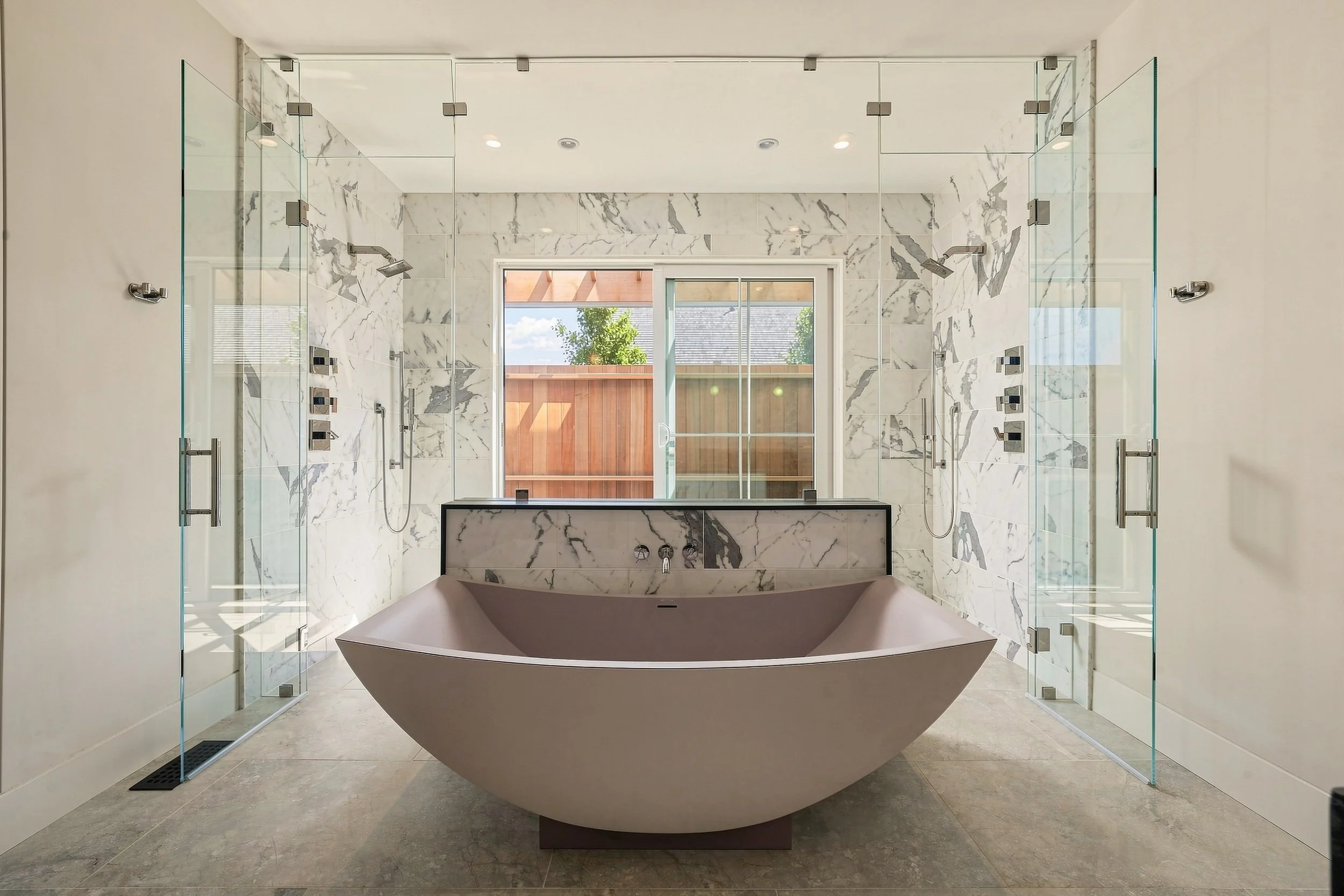 Primary bathroom with a sculptural soaking tub centered between two glass-enclosed marble showers