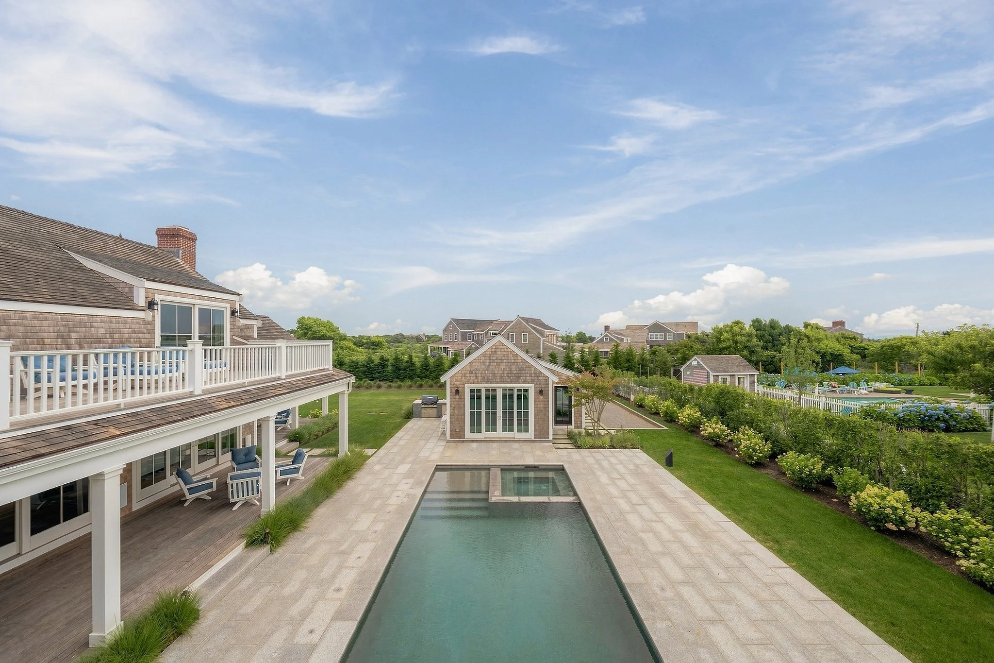 Elevated view along the swimming pool toward the cedar-shingle pool house and landscaped yard