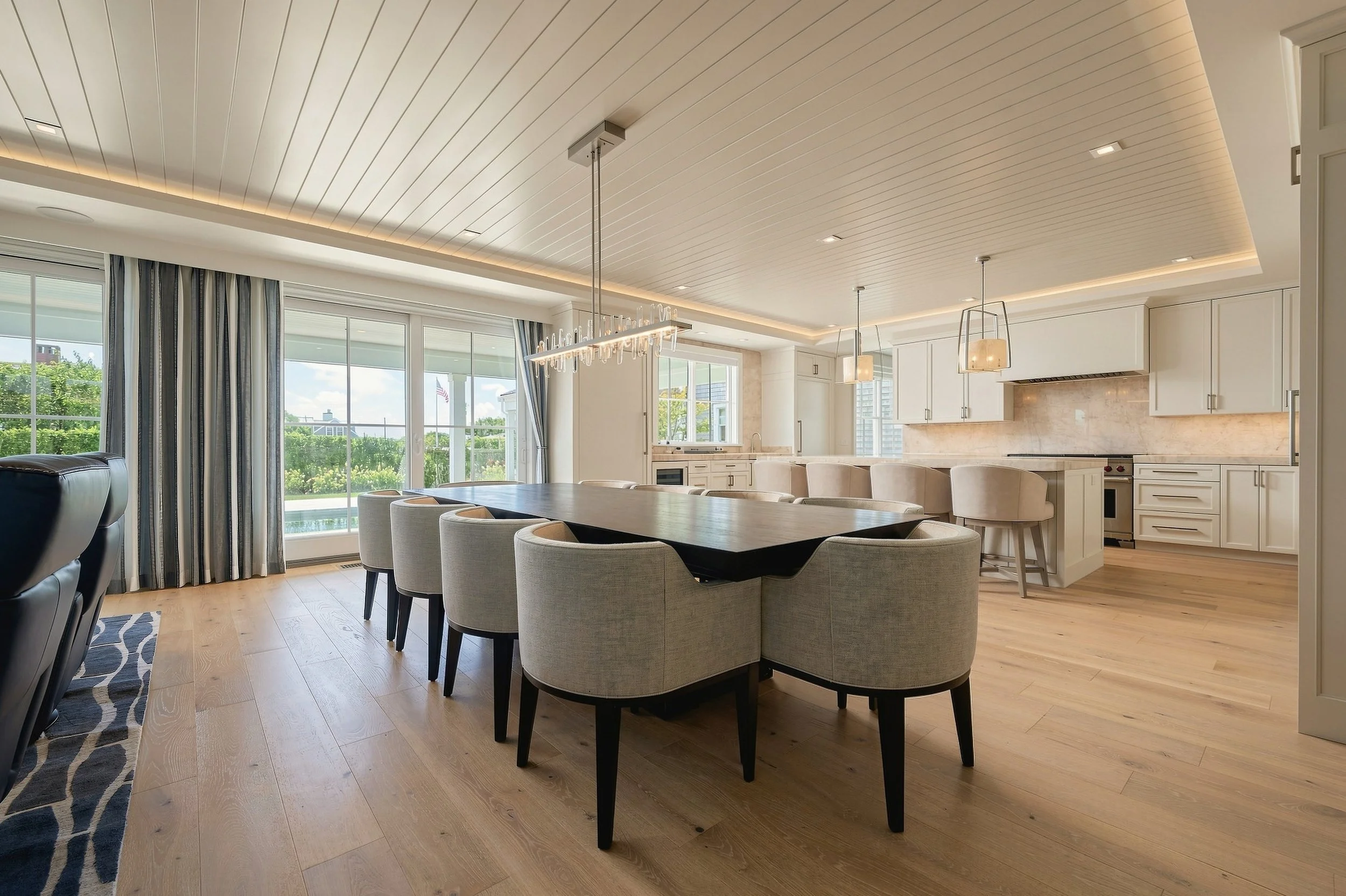 Dining area opening to a white kitchen with pendant lights, pale oak floors and a coffered ceiling