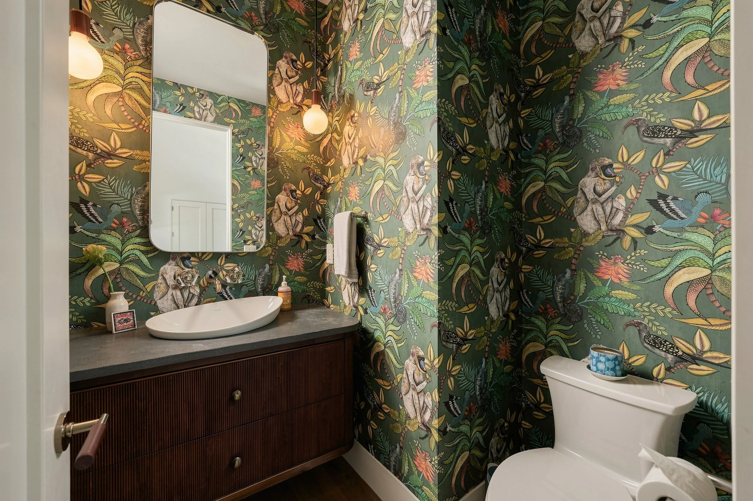 Powder room with botanical monkey wallpaper, a wood vanity and a white vessel sink