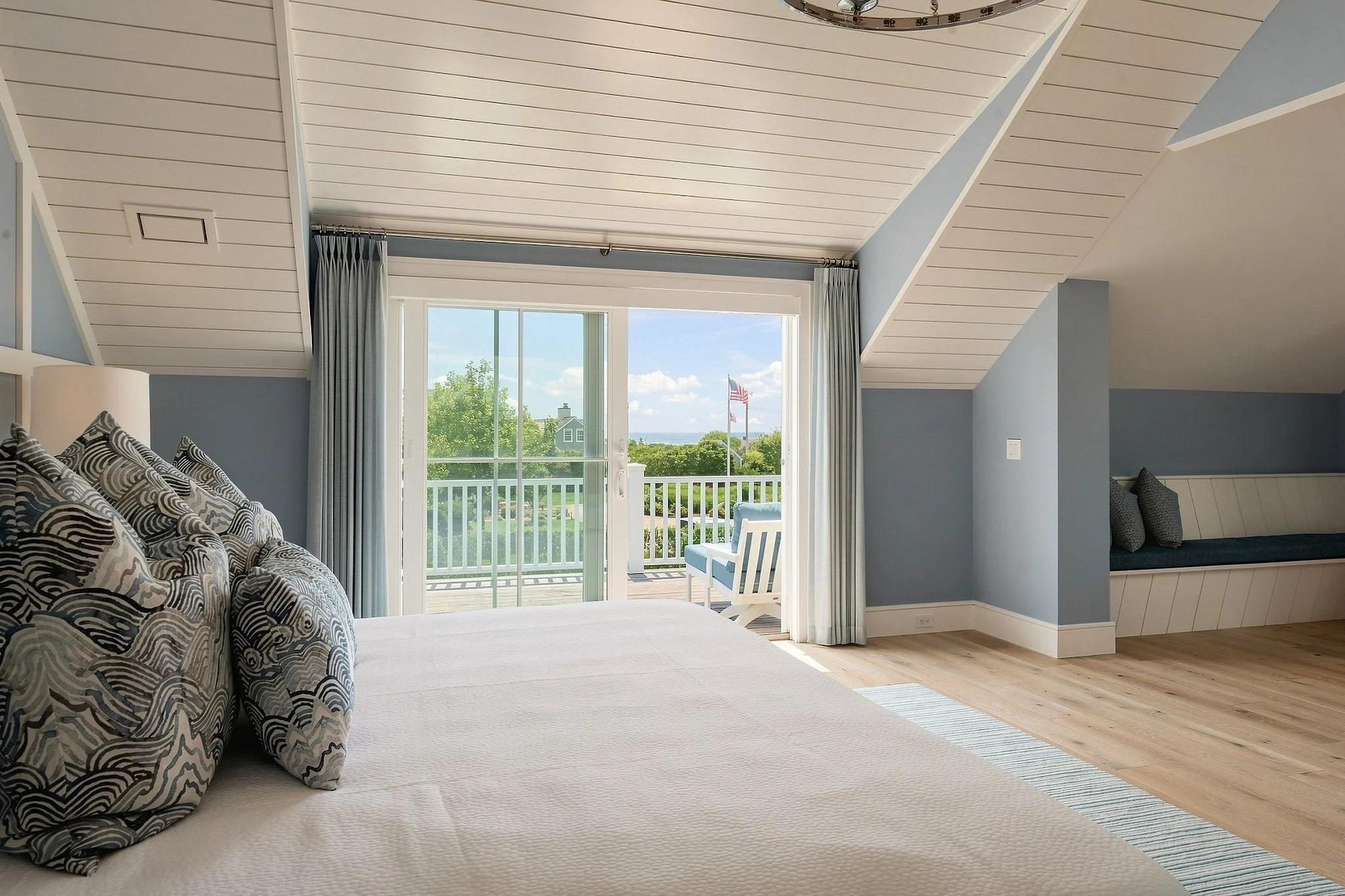 Coastal bedroom with blue walls, patterned pillows, a built-in window seat and balcony doors