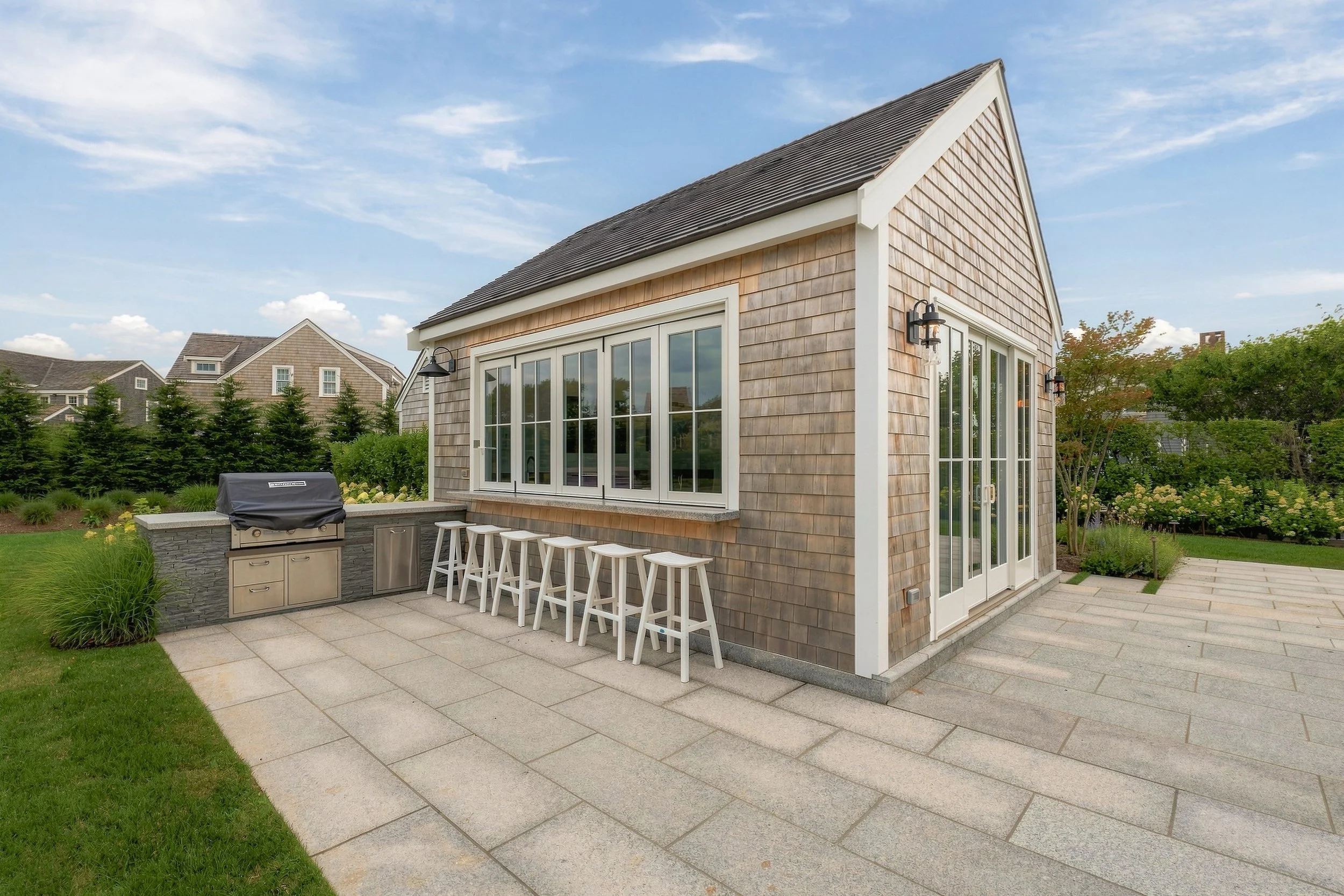 Cedar-shingle pool house with an outdoor grill, stone counter and five bar stools