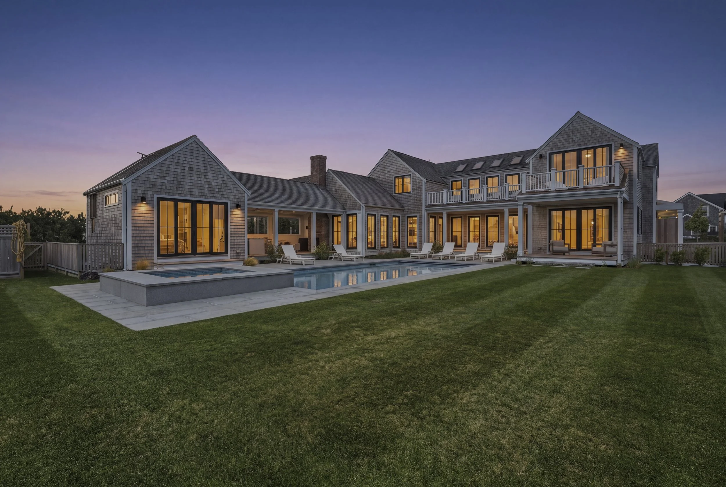 Twilight view of the illuminated cedar-shingle Sconset residence, swimming pool and spa in Nantucket