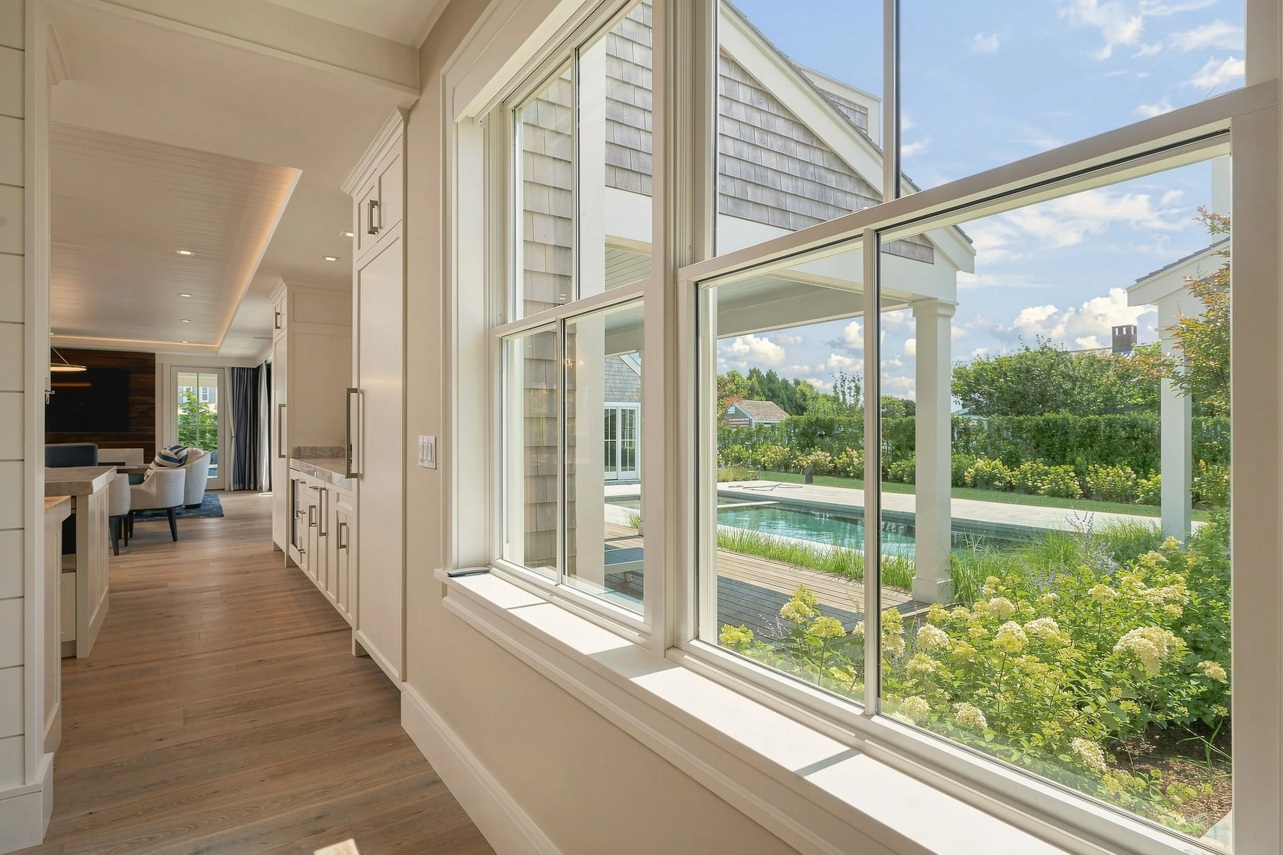 Bright hallway with large windows overlooking the pool, hydrangeas and cedar-shingle exterior