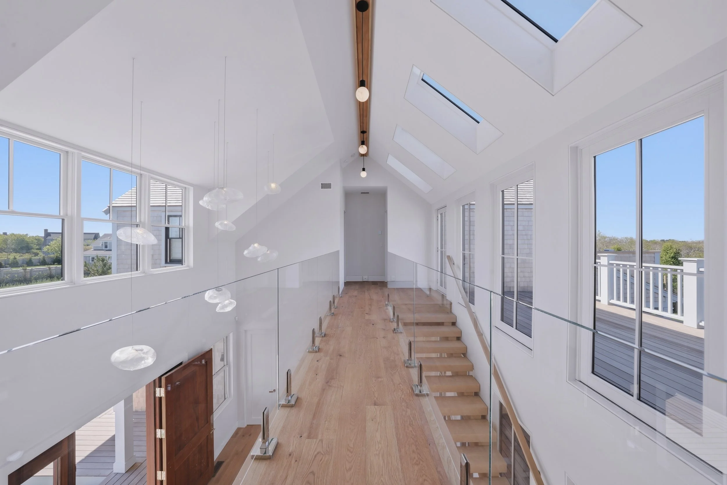 Upper landing with glass railings, oak floors, skylights and a sculptural pendant installation