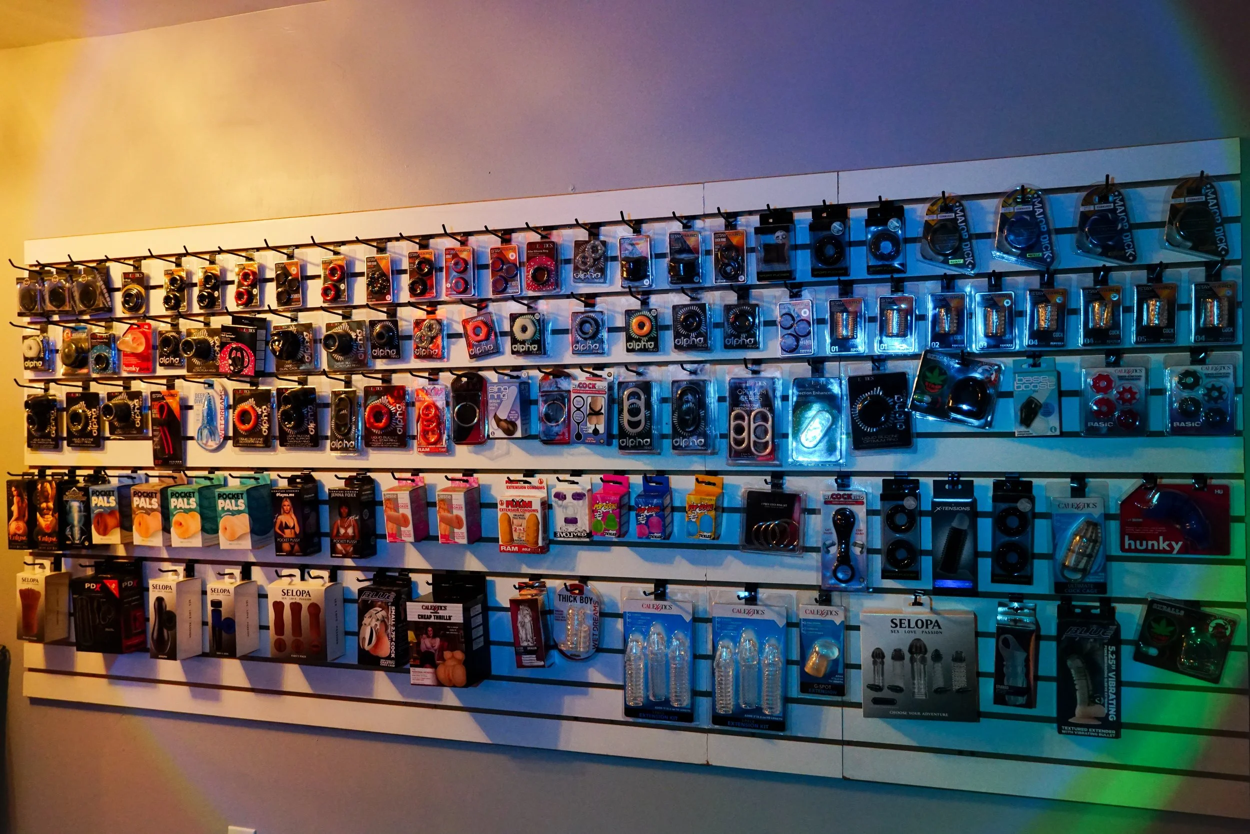 Display of various adult toys and accessories arranged on a wall with hooks in a store.