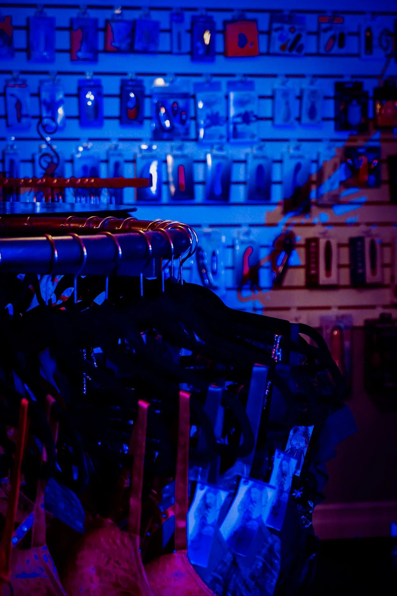 Clothing items hanging on a rack in a store with blue and red lighting, with a wall of packaged products in the background.