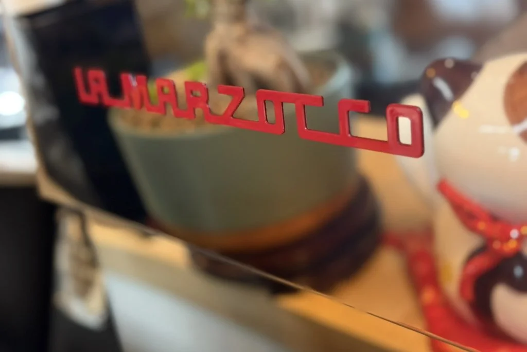 Close-up of the reflective surface of an espresso machine with the word 'Marzocco' written in red.