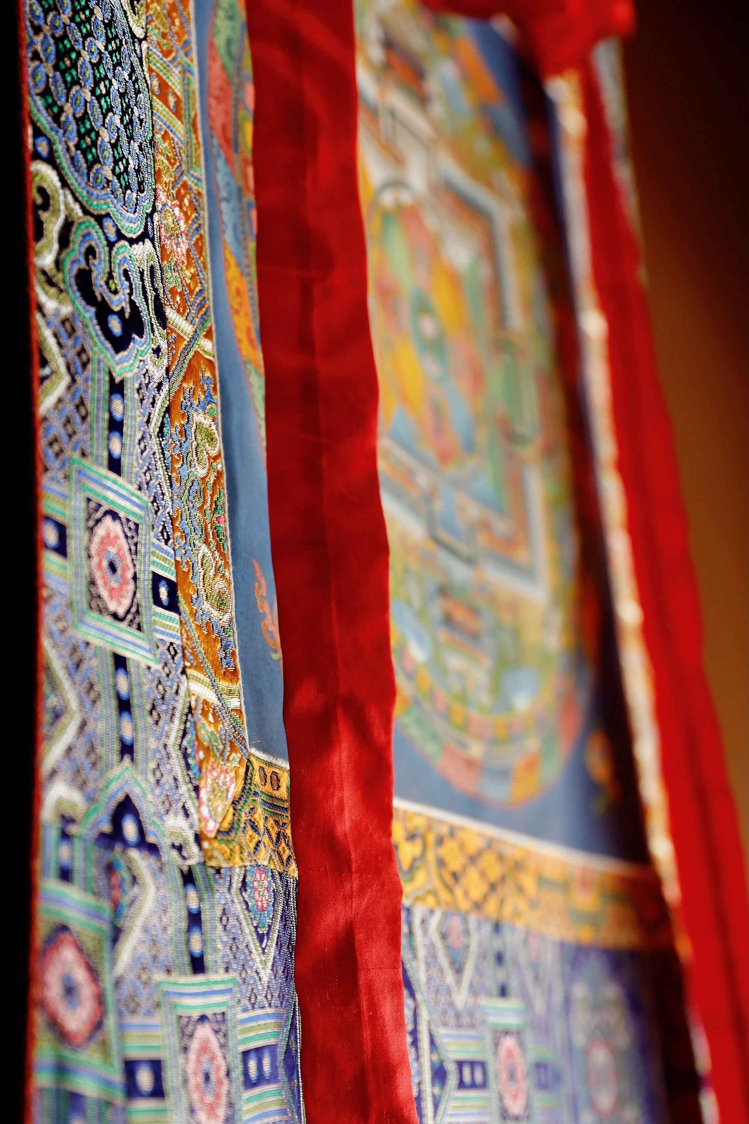 Colorful, intricate embroidered tapestry or cloth with geometric patterns and red fabric borders.