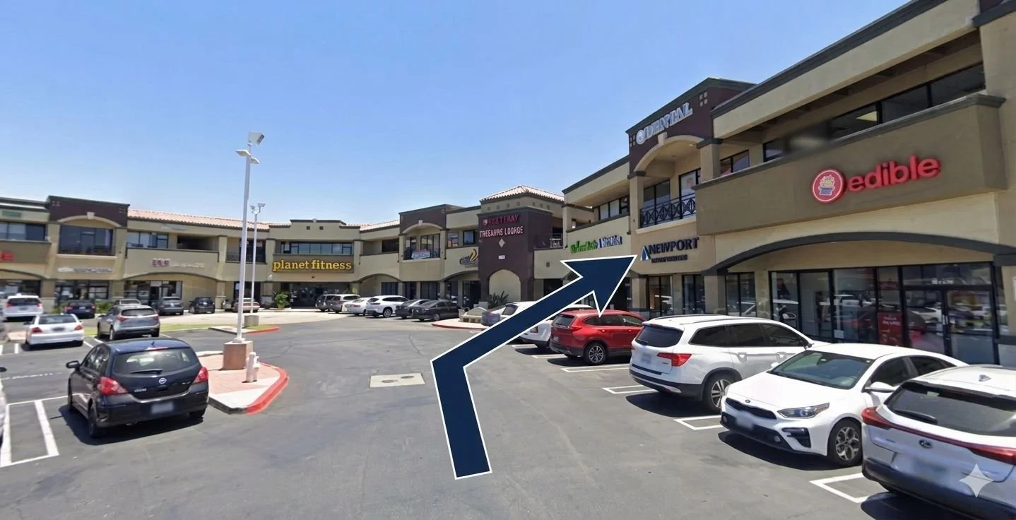 A parking lot in front of a strip mall with signs for stores like planet fitness, edible, and Newport. An arrow graphic points to the right, indicating a turn in the direction of the stores.