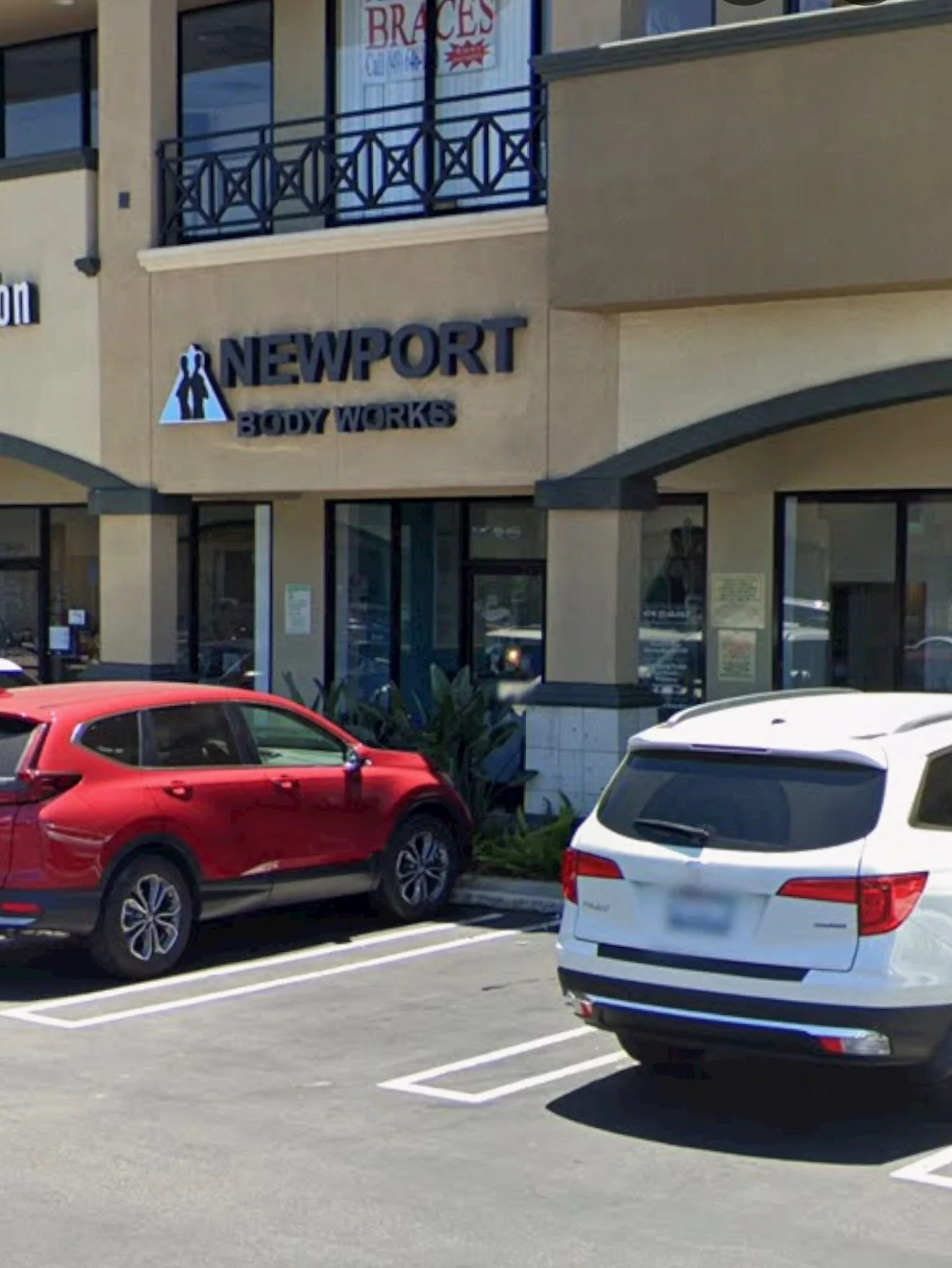 Exterior view of a retail store with the sign 'Newport Body Works' and parked cars in front, including a red vehicle and a white SUV.