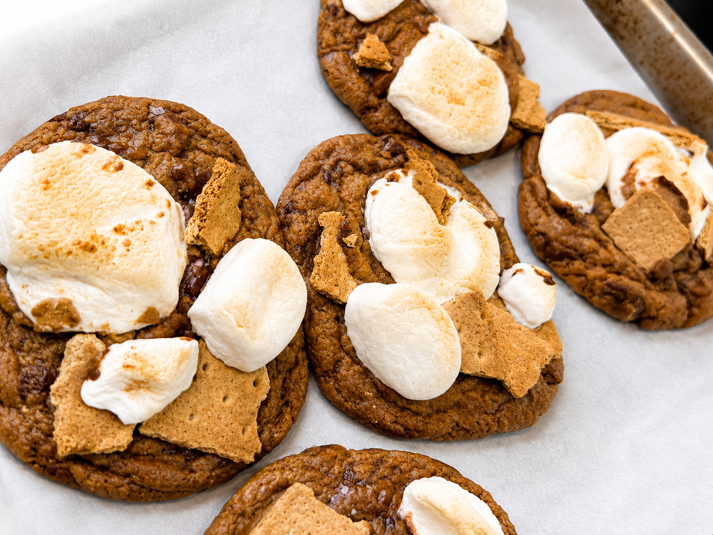 Close-up of homemade cookies with marshmallows, graham crackers, and chocolate chunks on parchment paper.