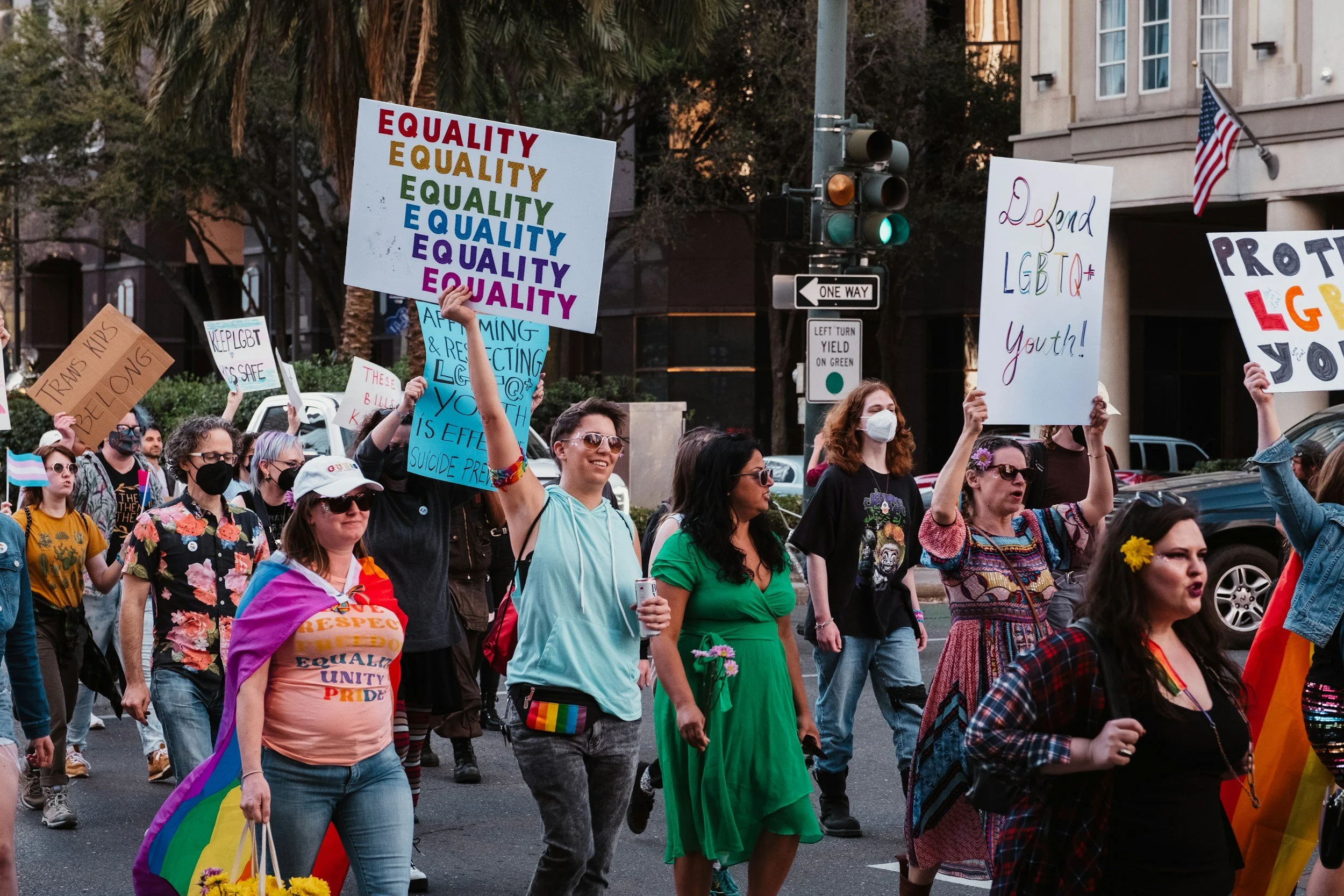 Group of diverse people participating in a LGBTQ+ pride march, holding signs advocating for equality, LGBTQ+ rights, and celebrating pride, with some wearing rainbow accessories and flags.