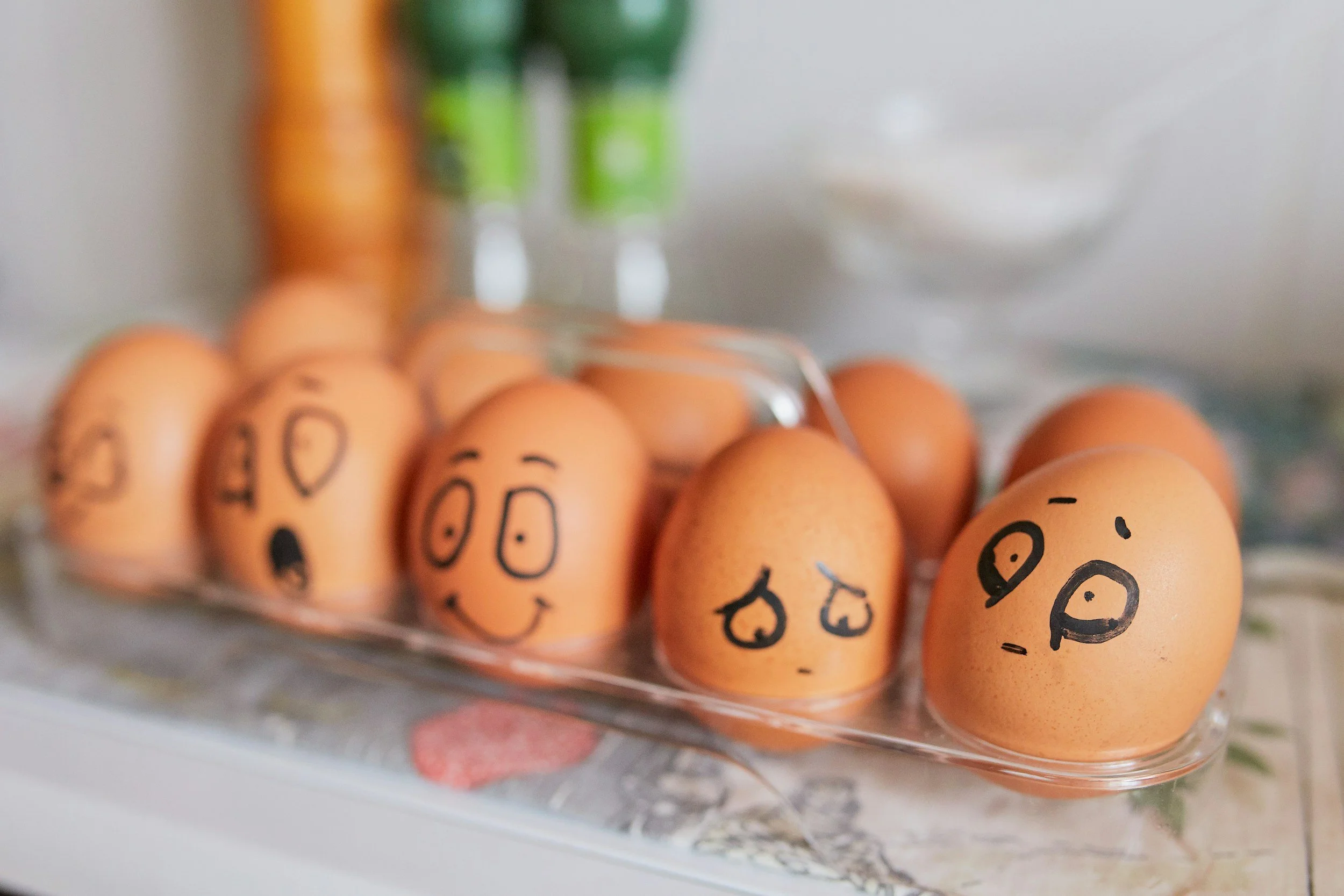 Eggs with faces drawn on them, placed in a plastic egg carton on a table.