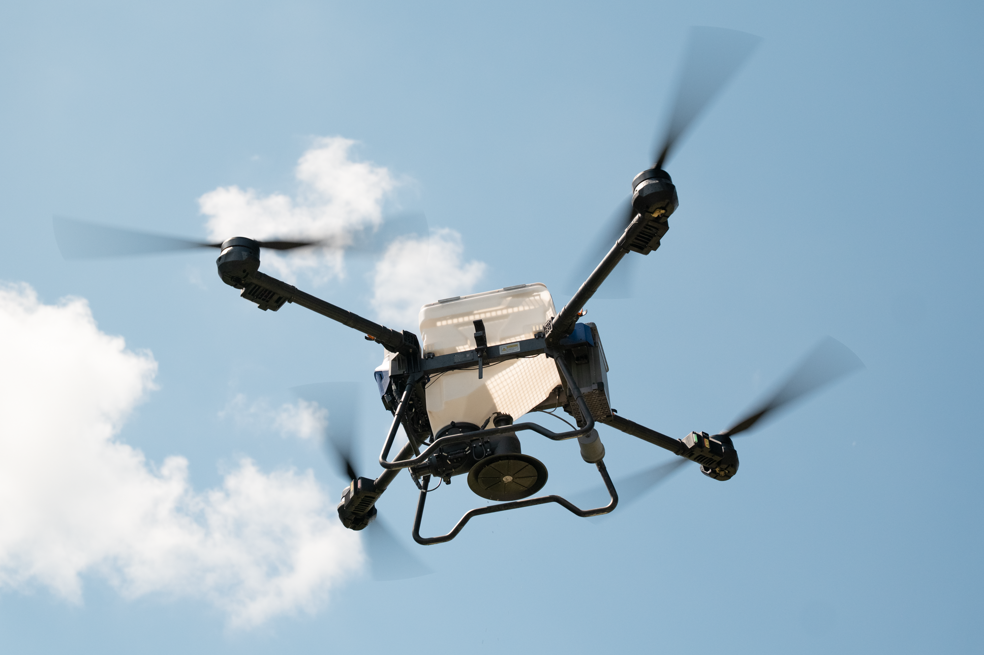 A drone flying in the sky with four spinning propellers.