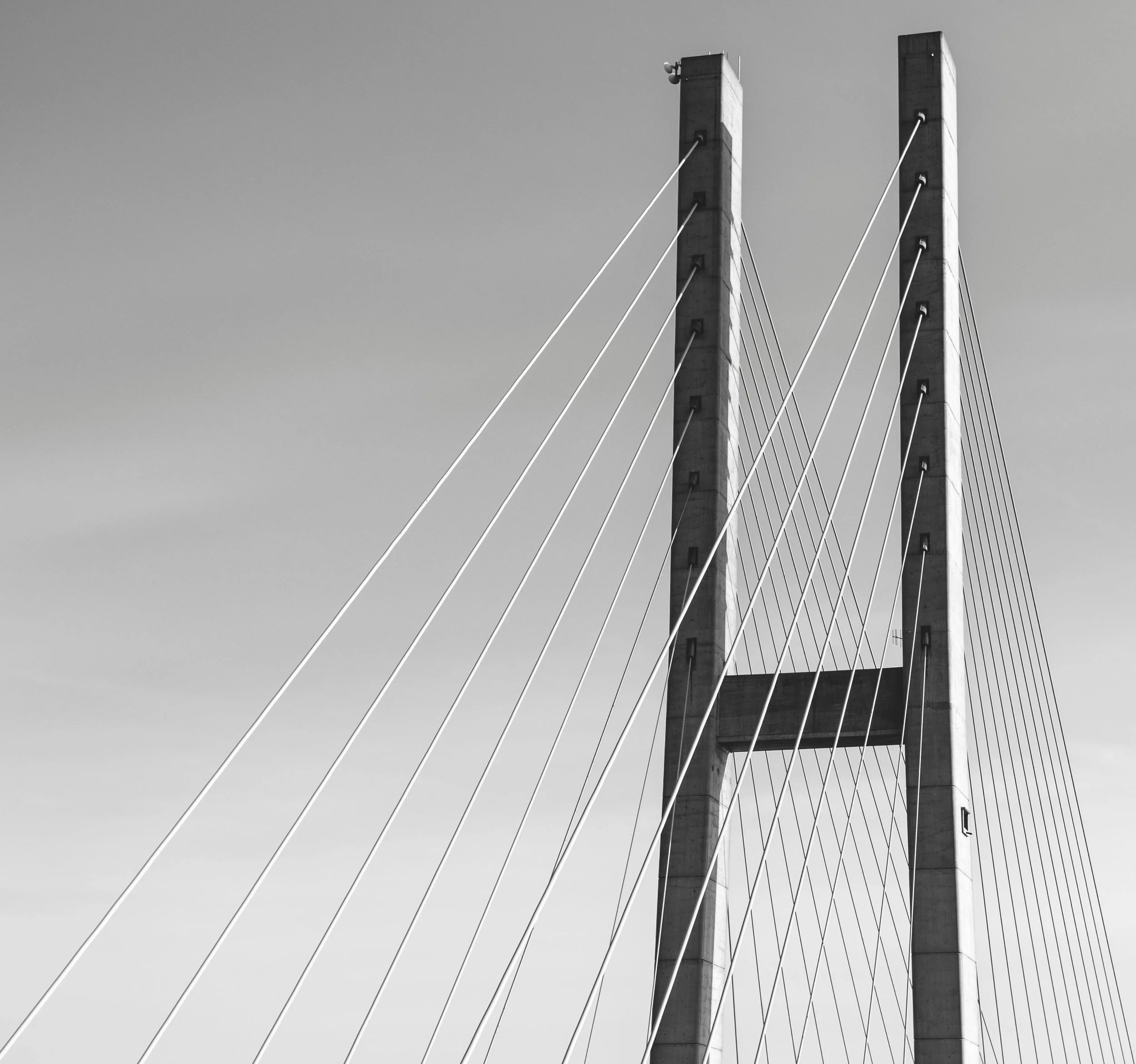 Black and white photo of a modern cable-stayed bridge with two tall towers and multiple cables supporting the roadway against a cloudy sky.