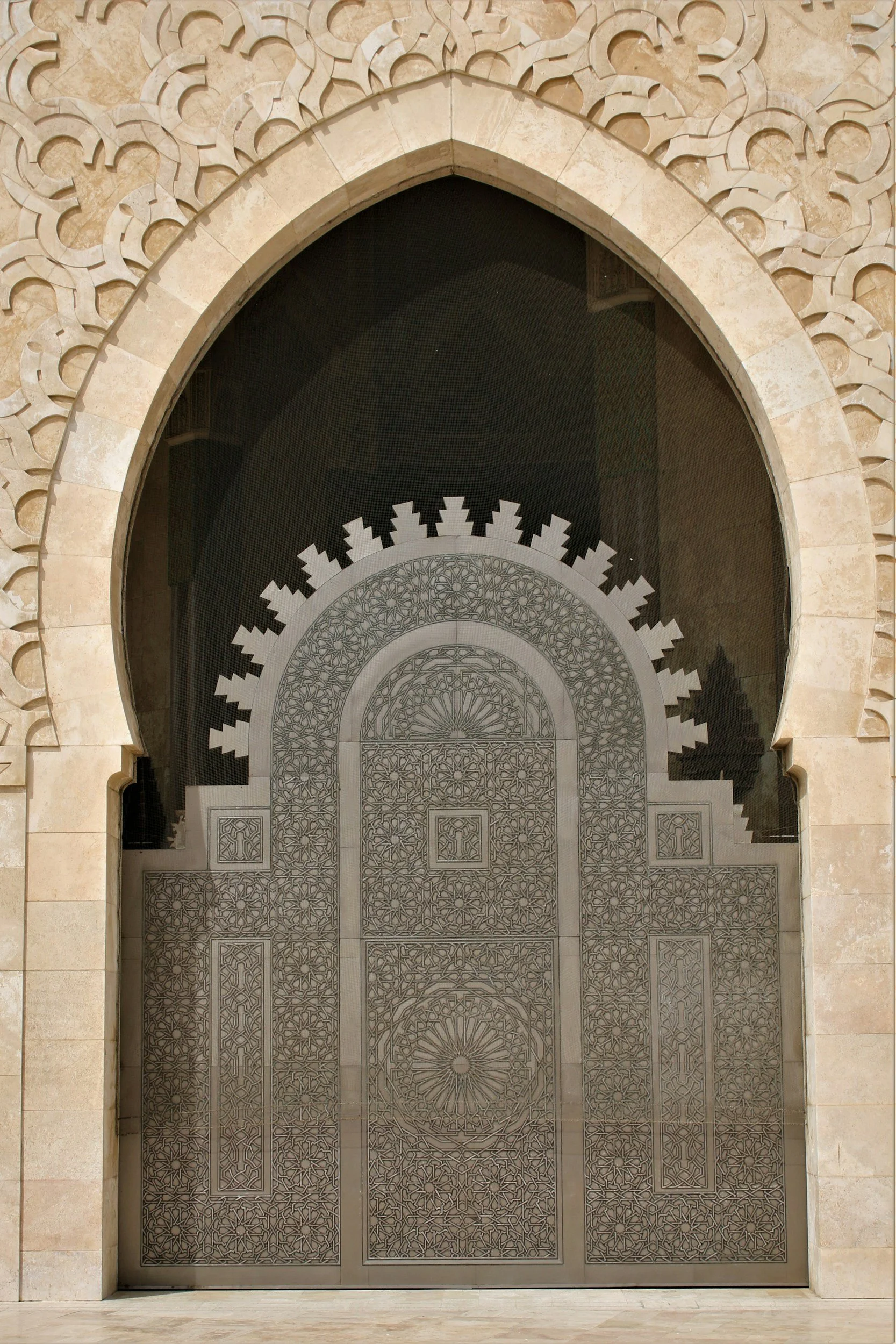 Decorative and intricately designed metal gate with geometric patterns, framed by an arched stone doorway with carved details.
