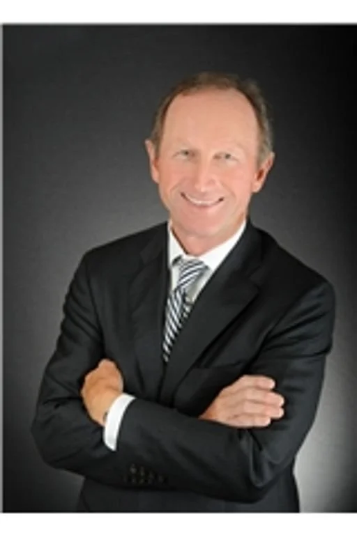 A smiling middle-aged man in a dark suit, white shirt, and striped tie, posing with arms crossed against a dark background. Social Media Management. Digital Marketing. Media Agency.