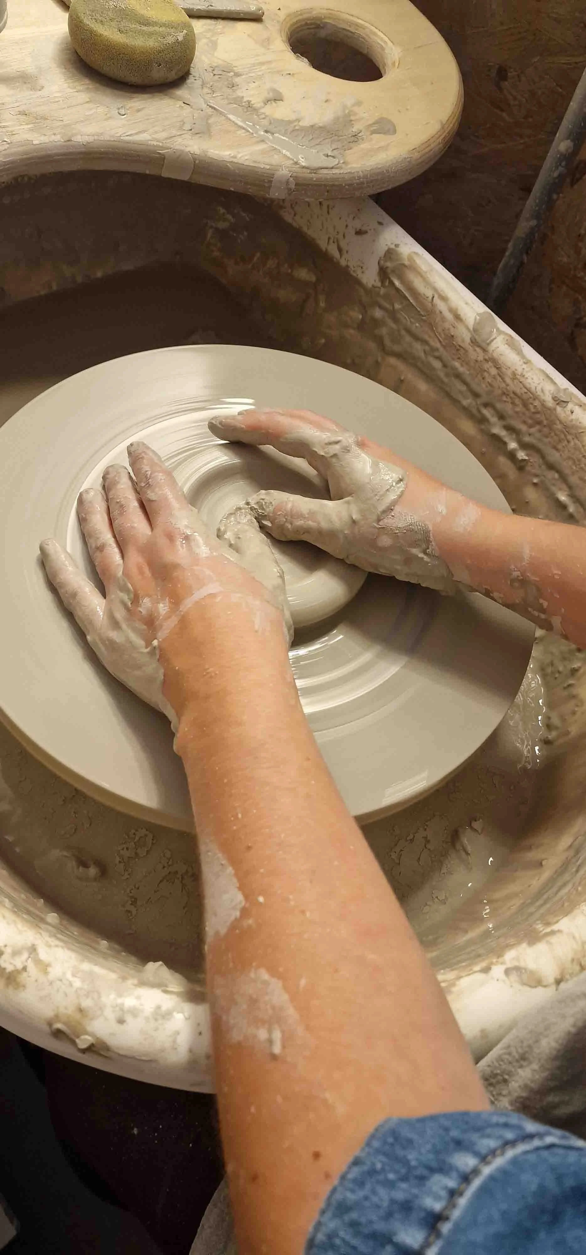 Hands shaping a clay bowl on a pottery wheel with white slip, in a pottery studio.