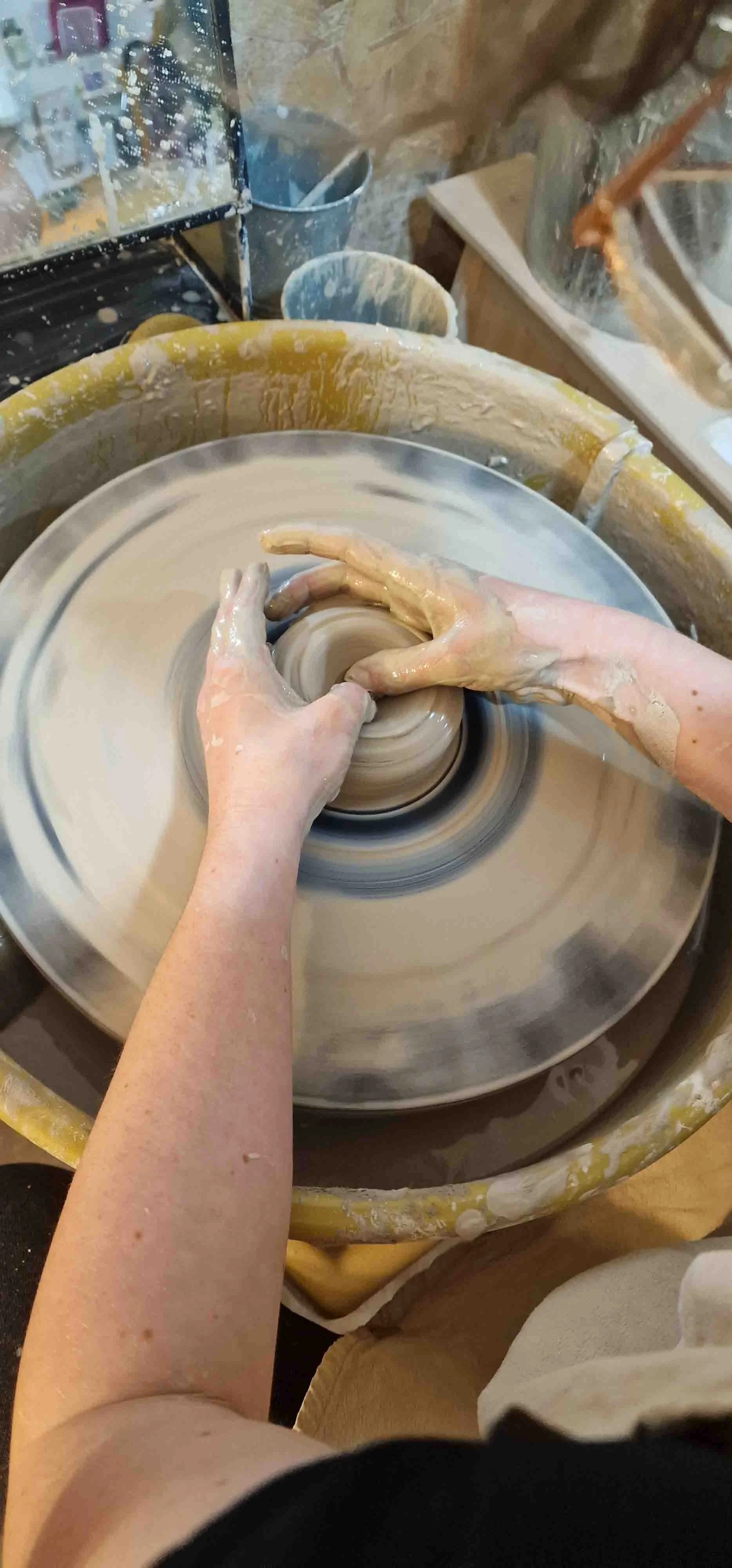 Person shaping a clay bowl on a pottery wheel in a ceramic studio.
