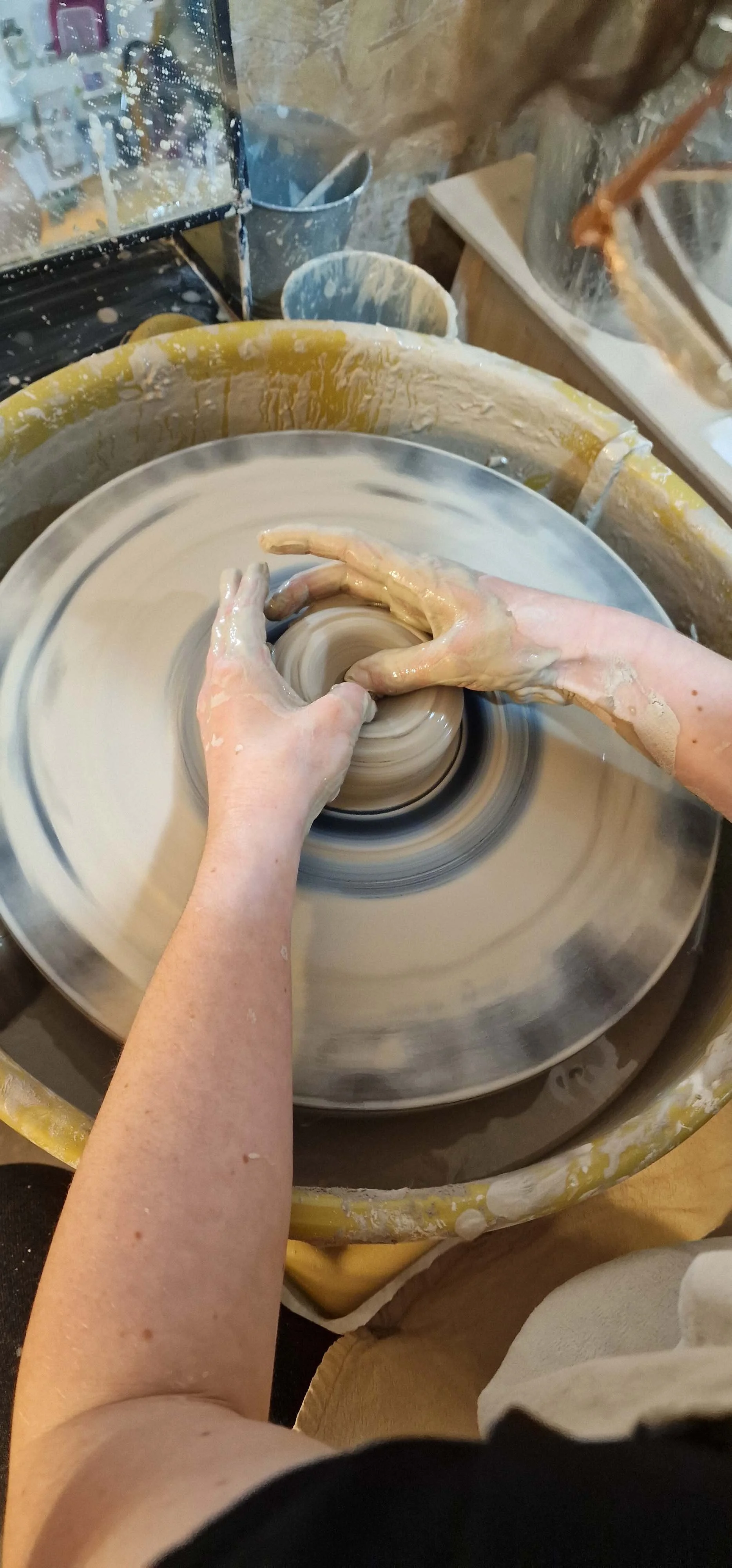 Person shaping clay on a pottery wheel in a ceramics studio.