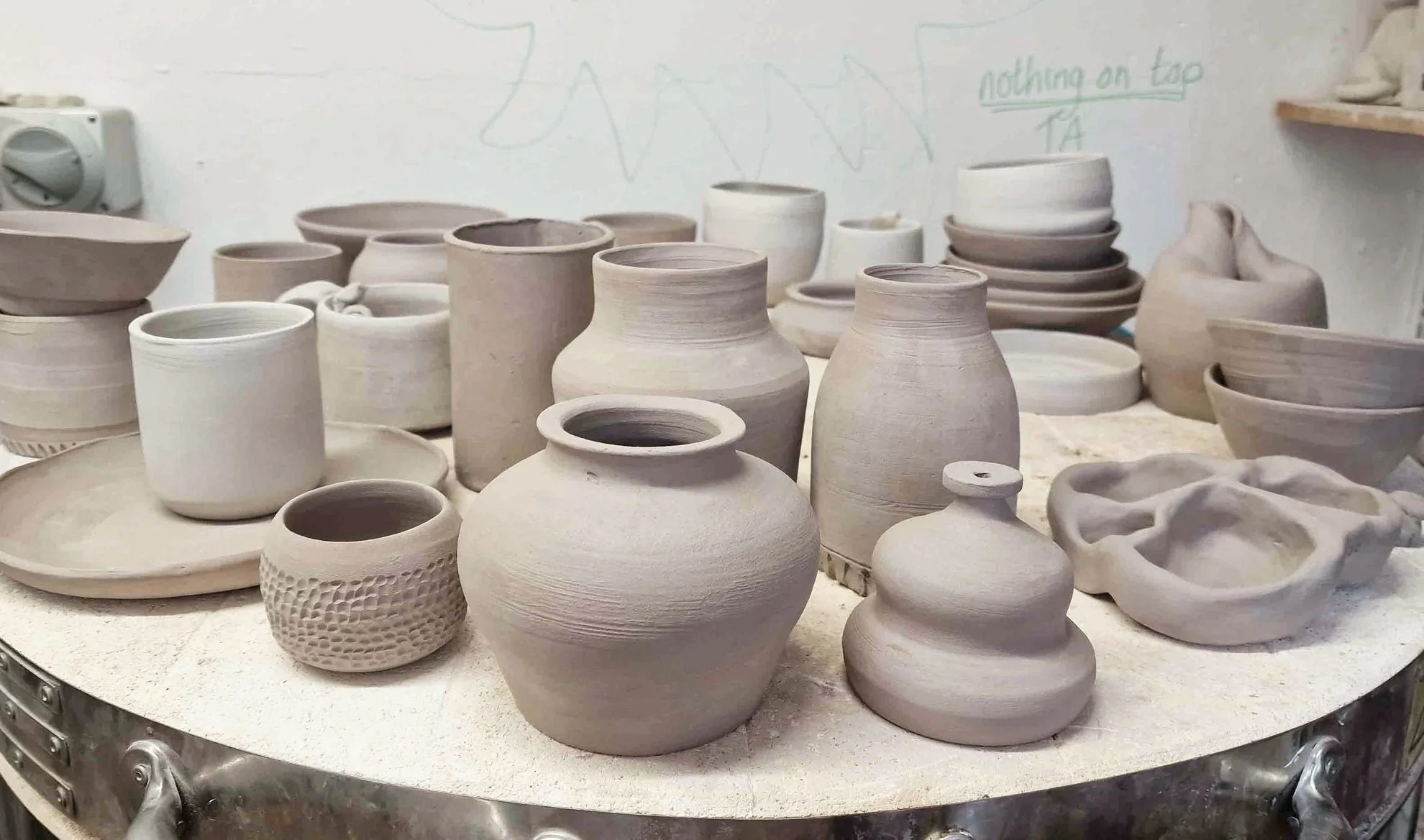 Various unglazed ceramic pots and bowls on a pottery wheel in a ceramic studio.
