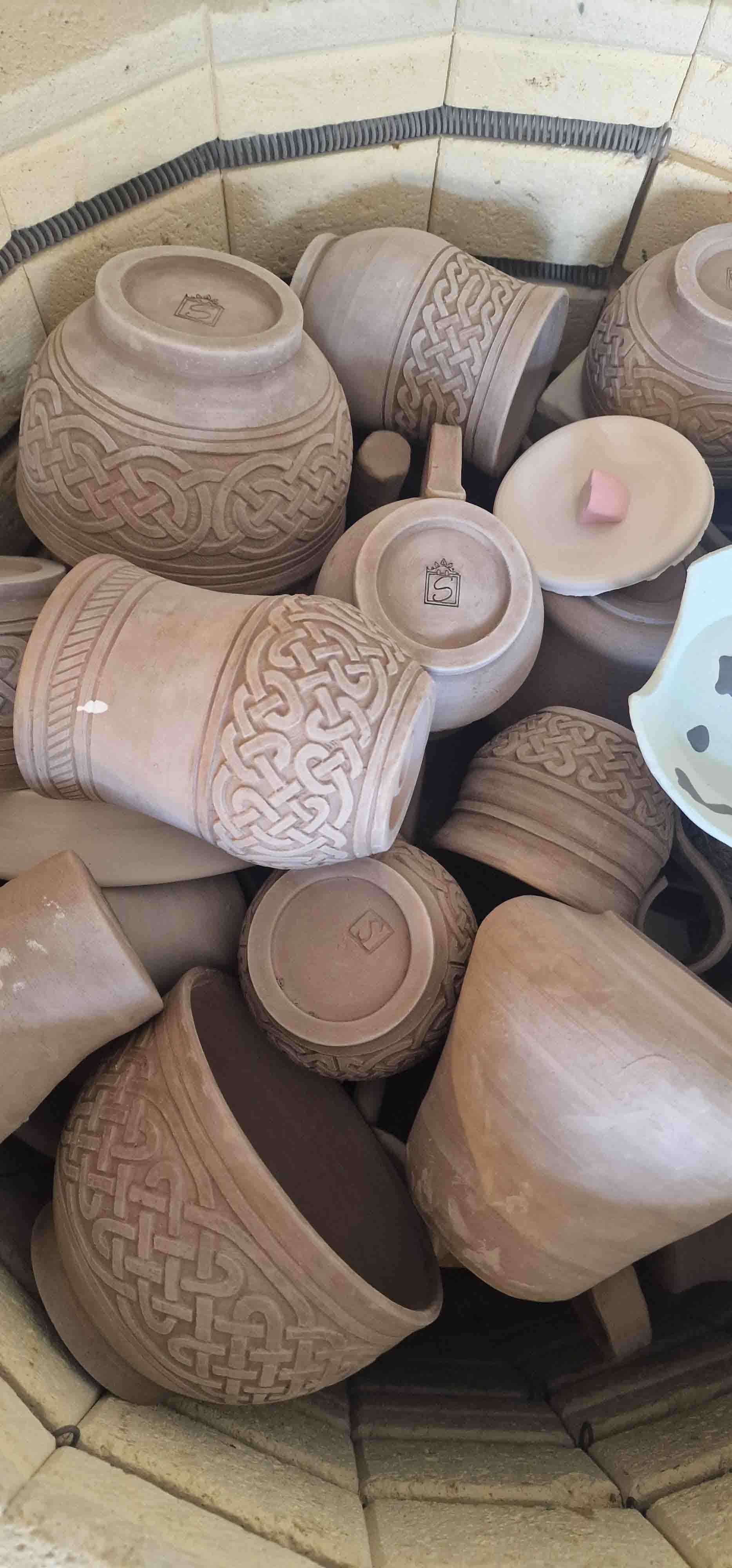 Several unfinished clay pots with intricate carvings and patterns, stacked inside a kiln.