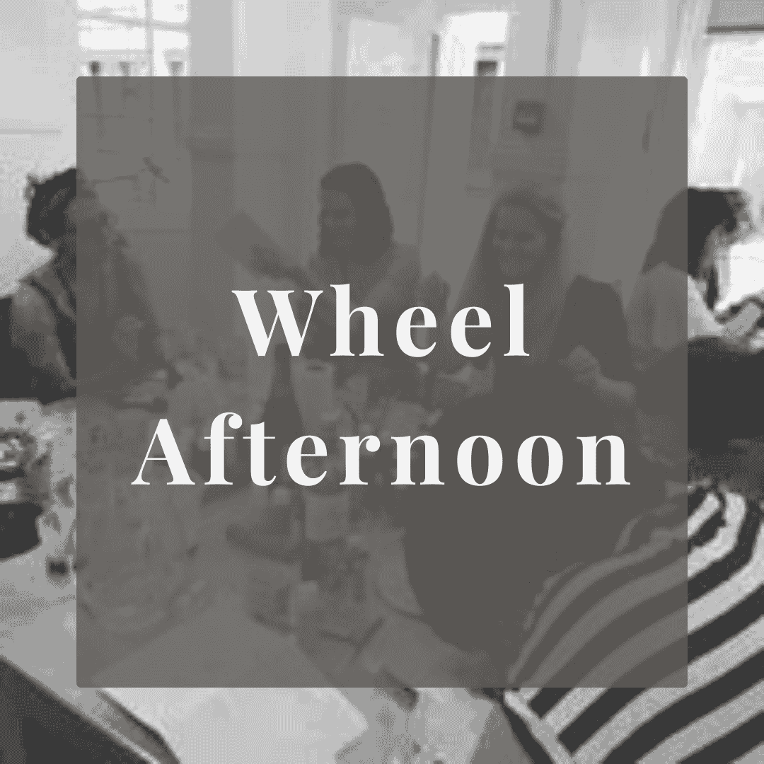 A group of people sitting around a table in an indoor setting, engaging in a conversation or activity. The image has a text overlay that reads 'Wheel Afternoon'.