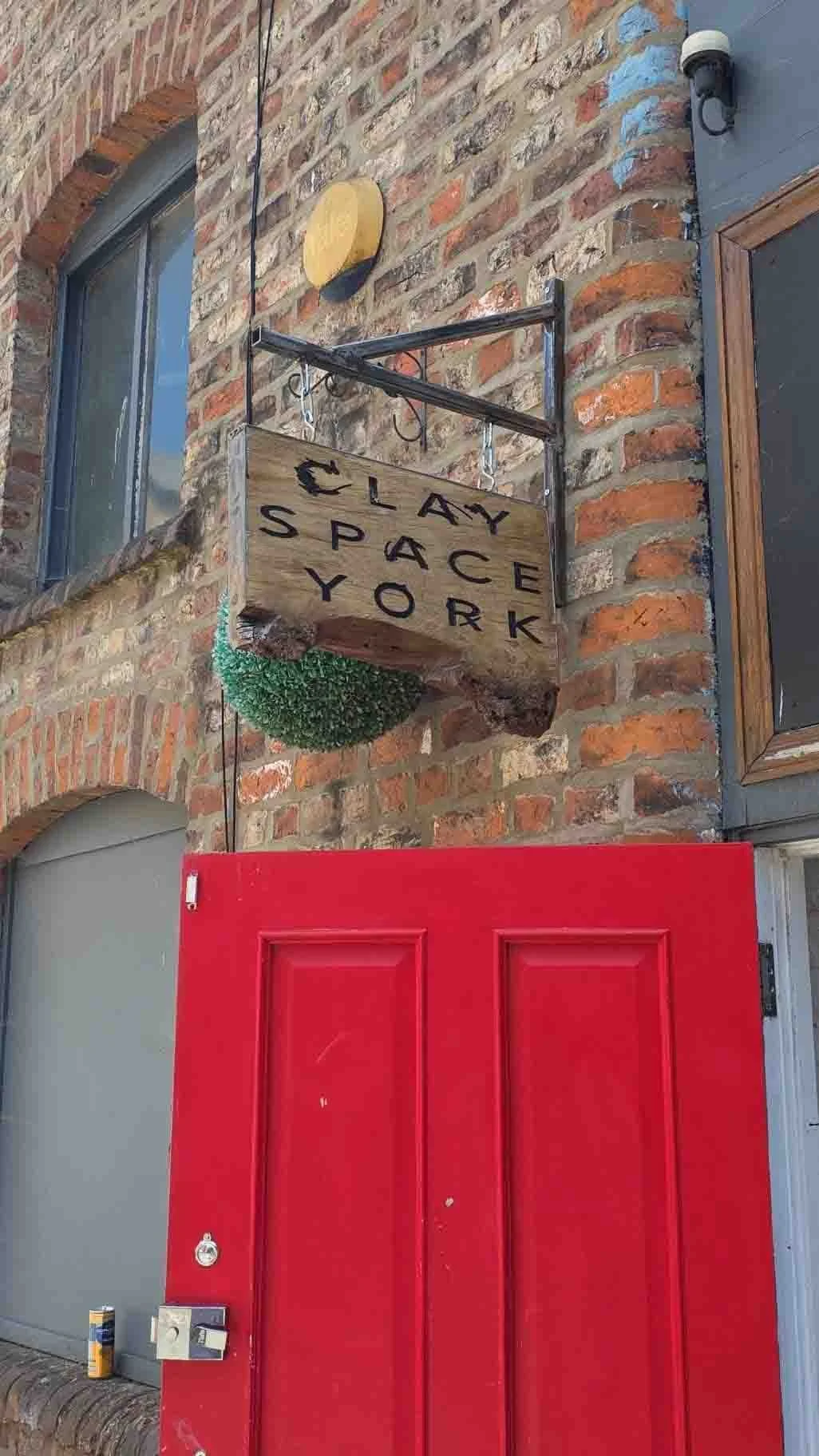 A sign reading 'Clay Space York' hangs above a red door on a brick building.