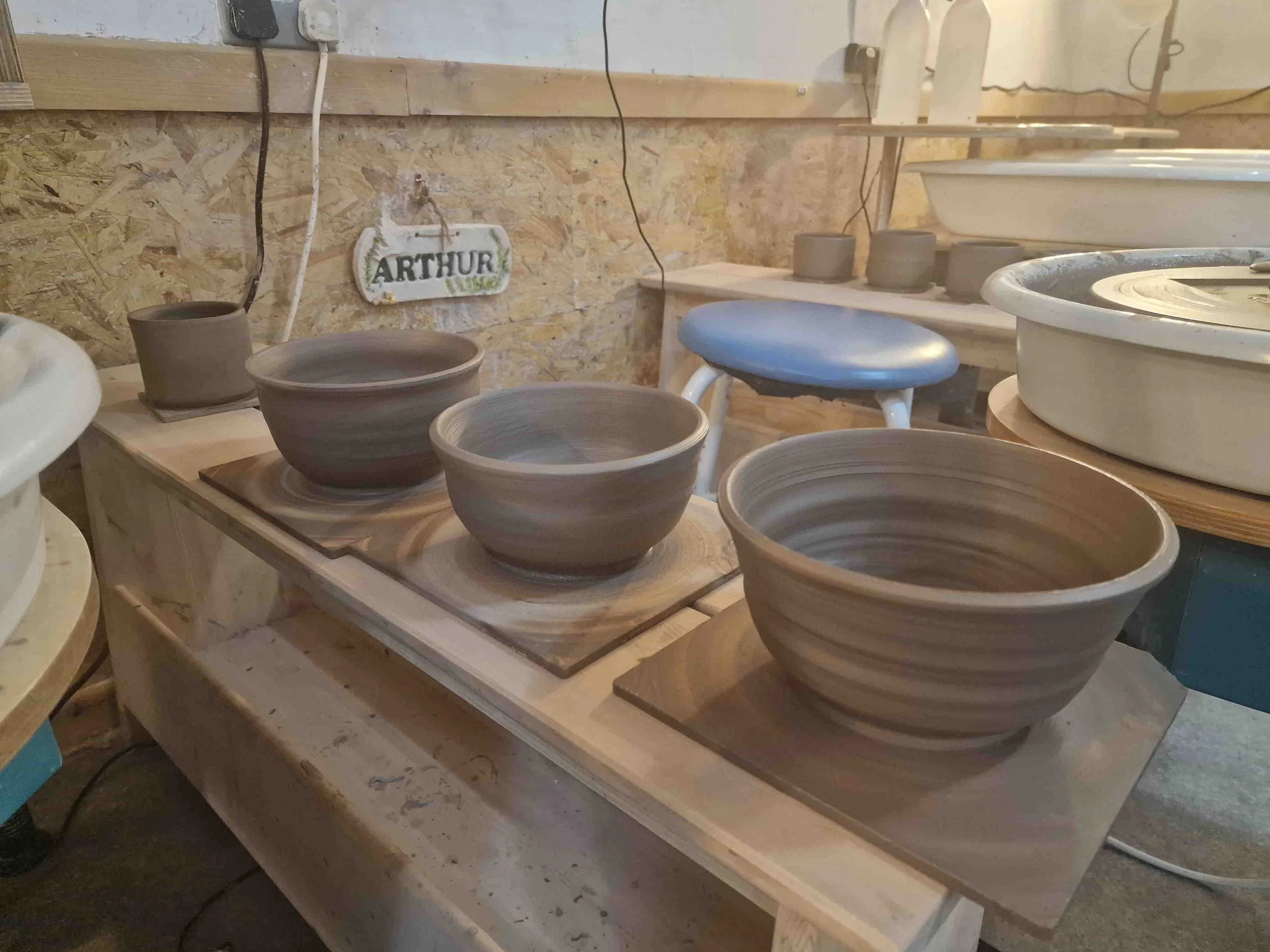 Clay bowls and pots being shaped on a pottery wheel in a ceramics studio.