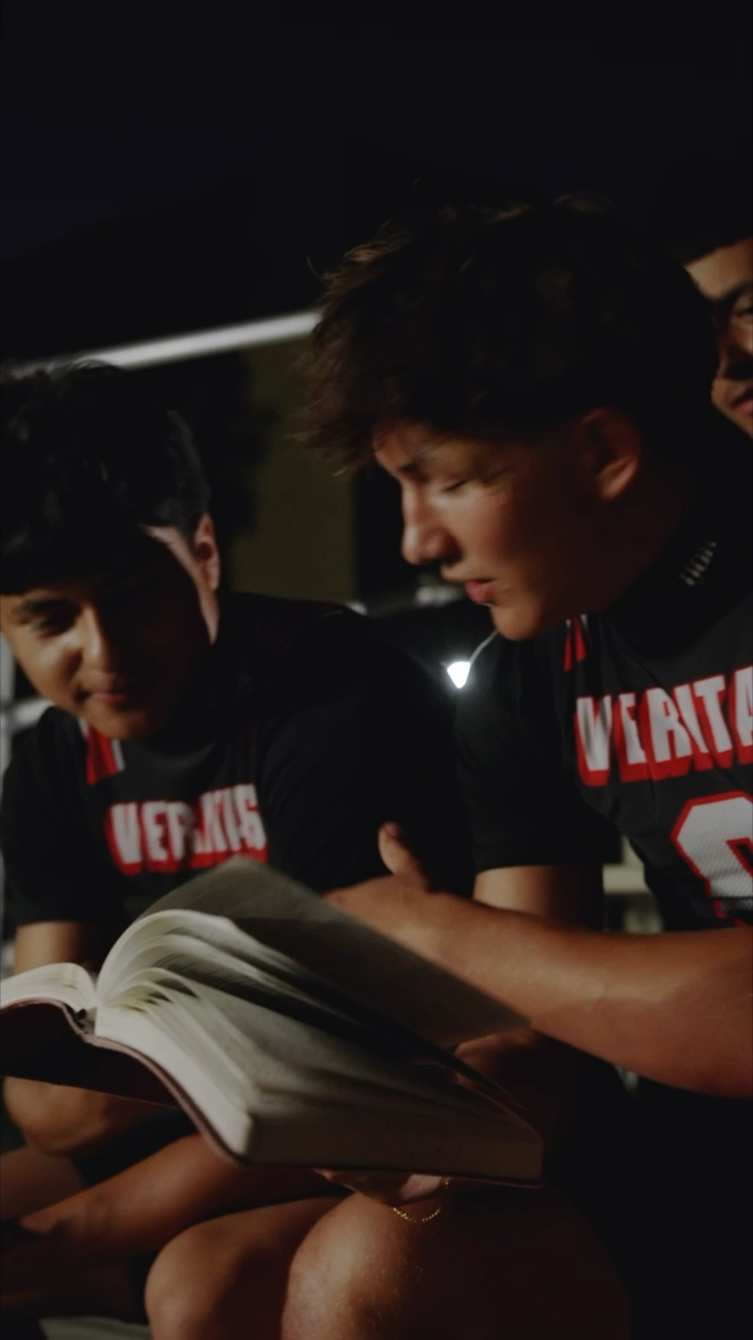 Veritas athletes in team jerseys reading an open Bible together