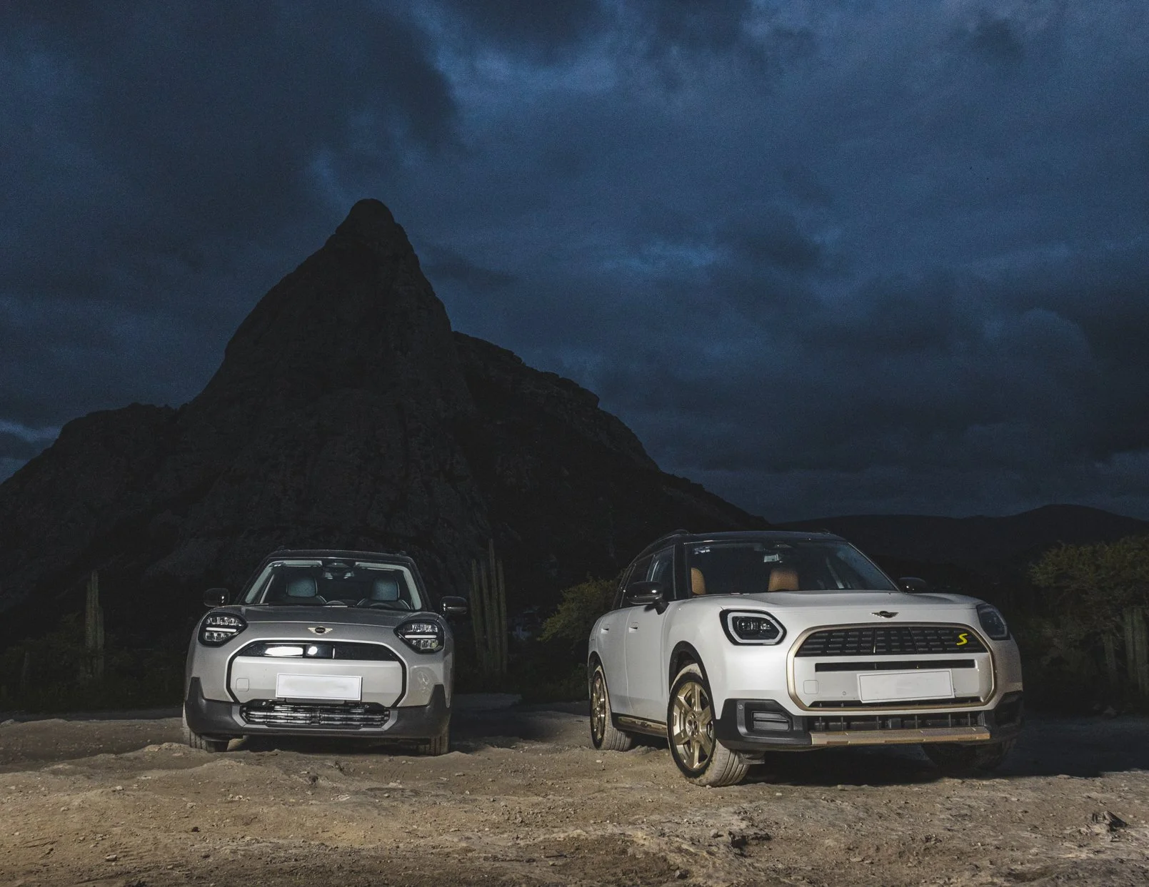 Dos autos nuevos estacionados en un camino de tierra con montaña en la noche.