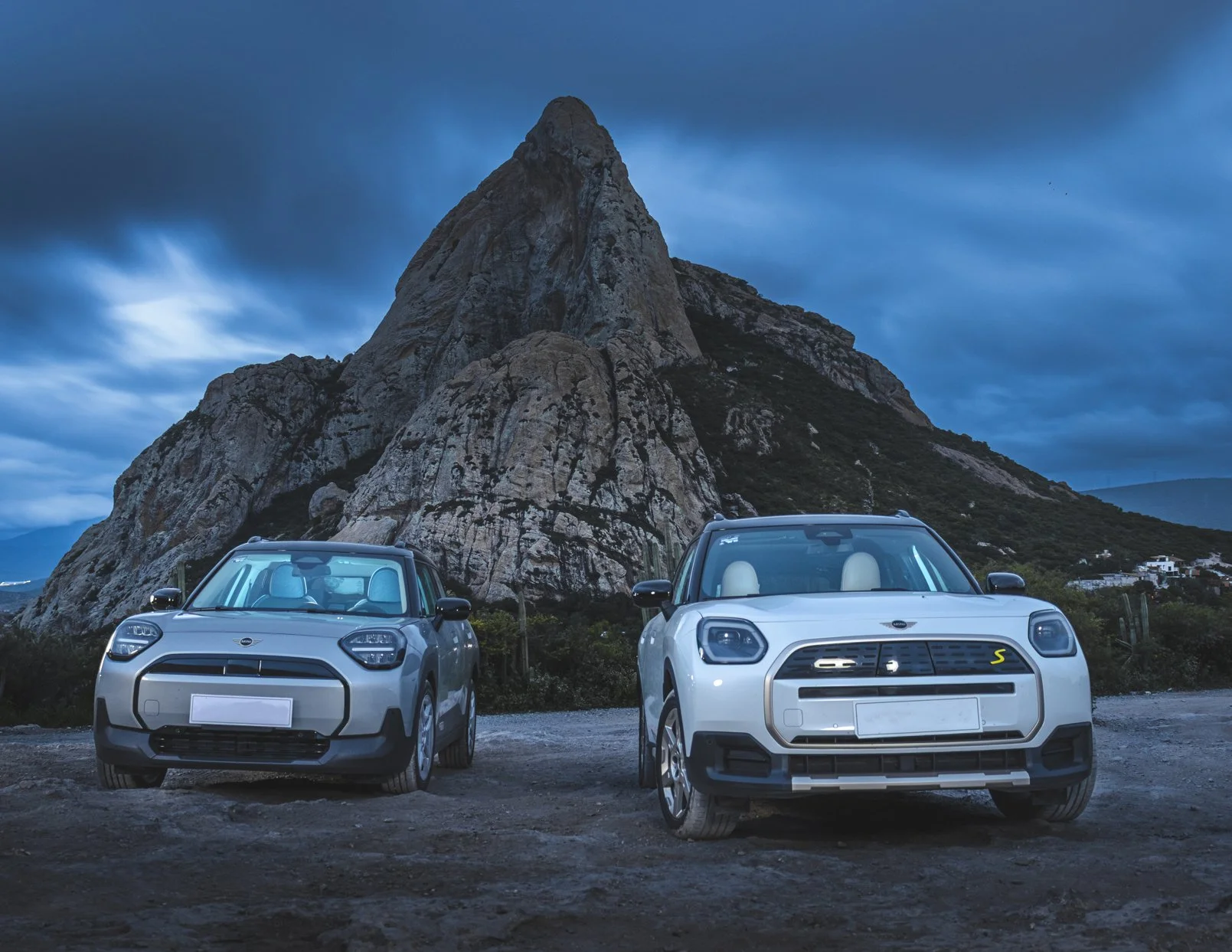 Dos autos modernos en un paisaje montañoso con cielo nublado.