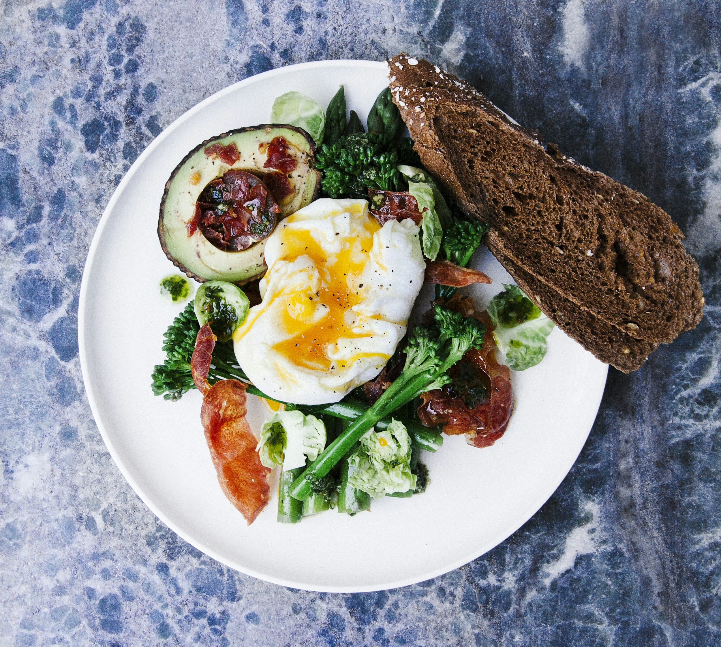 a plate of delicious looking food including a poached egg, avocado, greens, and spices