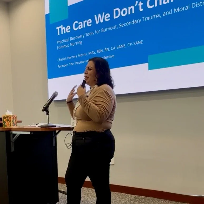 A woman holding a microphone and gesturing with her hands in front of a large presentation screen at a conference. The screen displays a presentation titled 'The Care We Don’t Char' with additional text about recovery tools for burnout, secondary trauma, and moral distress.