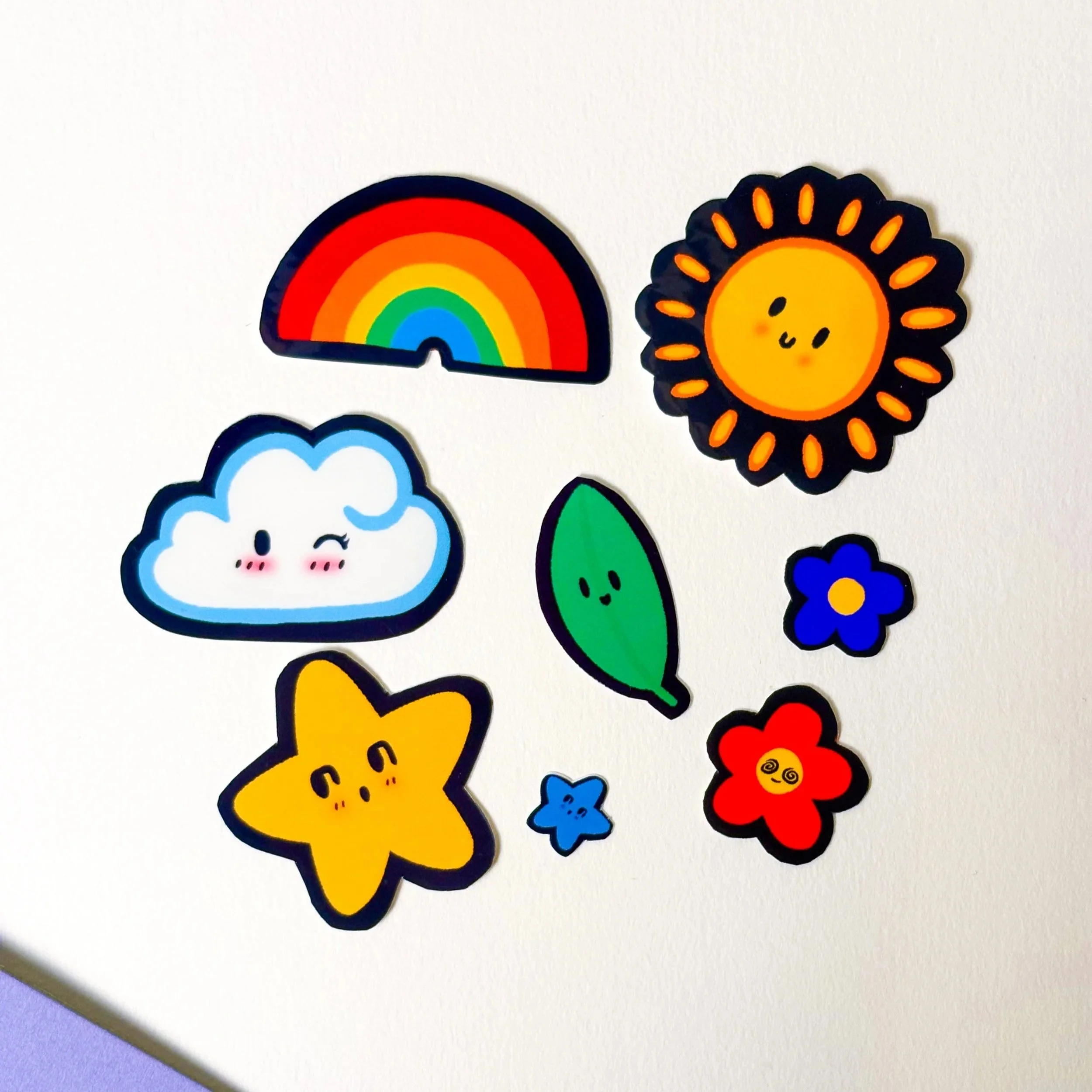 Colorful cartoon stickers of a rainbow, smiling sun, cloud, leaf, blue flower, red flower with a face, yellow star with a face, and two small stars, arranged on a plain white background.