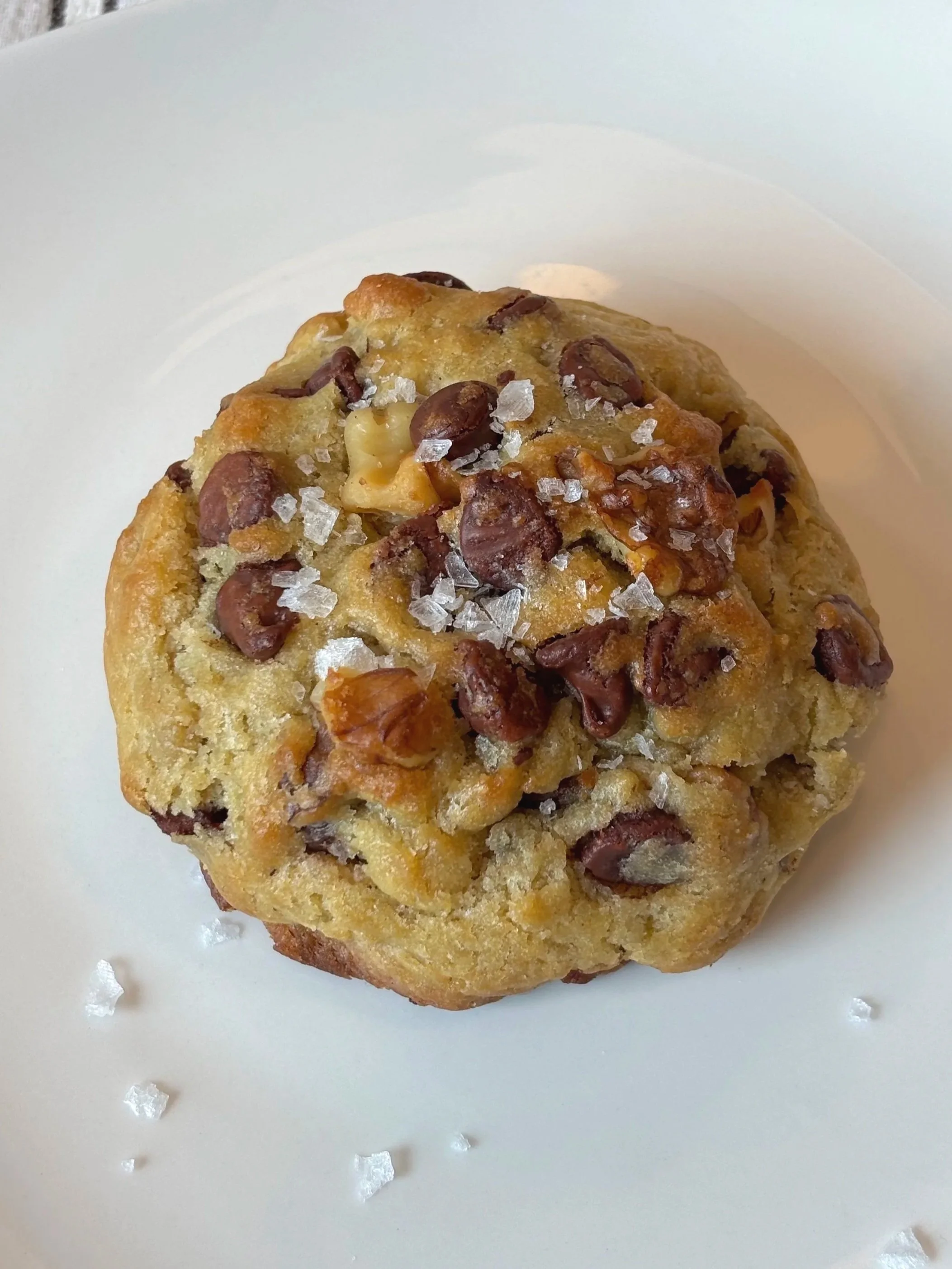 Hand holding a large chocolate chip cookie with walnuts, on a white marble surface.