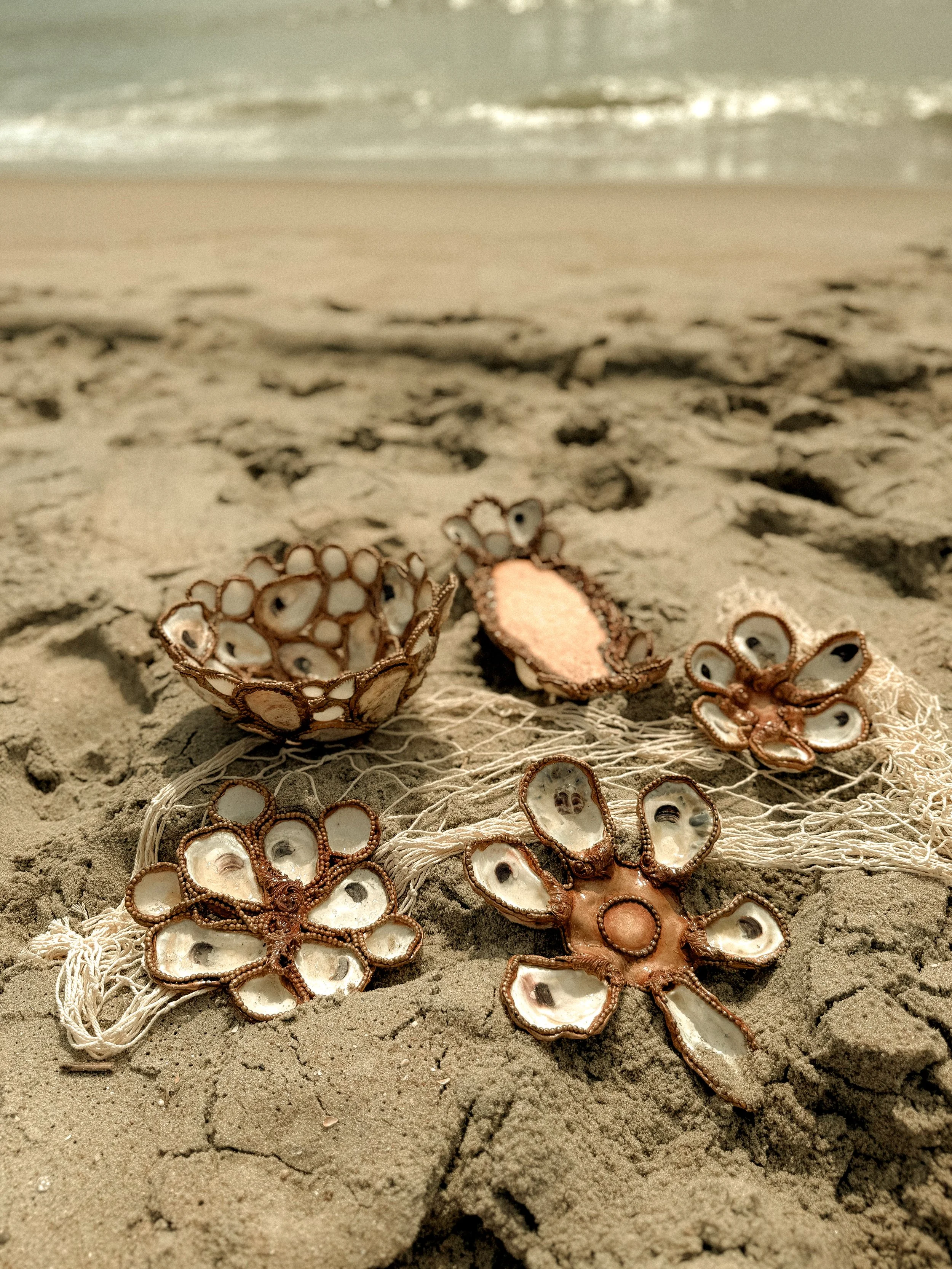 Decorative shell and fabric ornament on sandy beach with ocean in background.