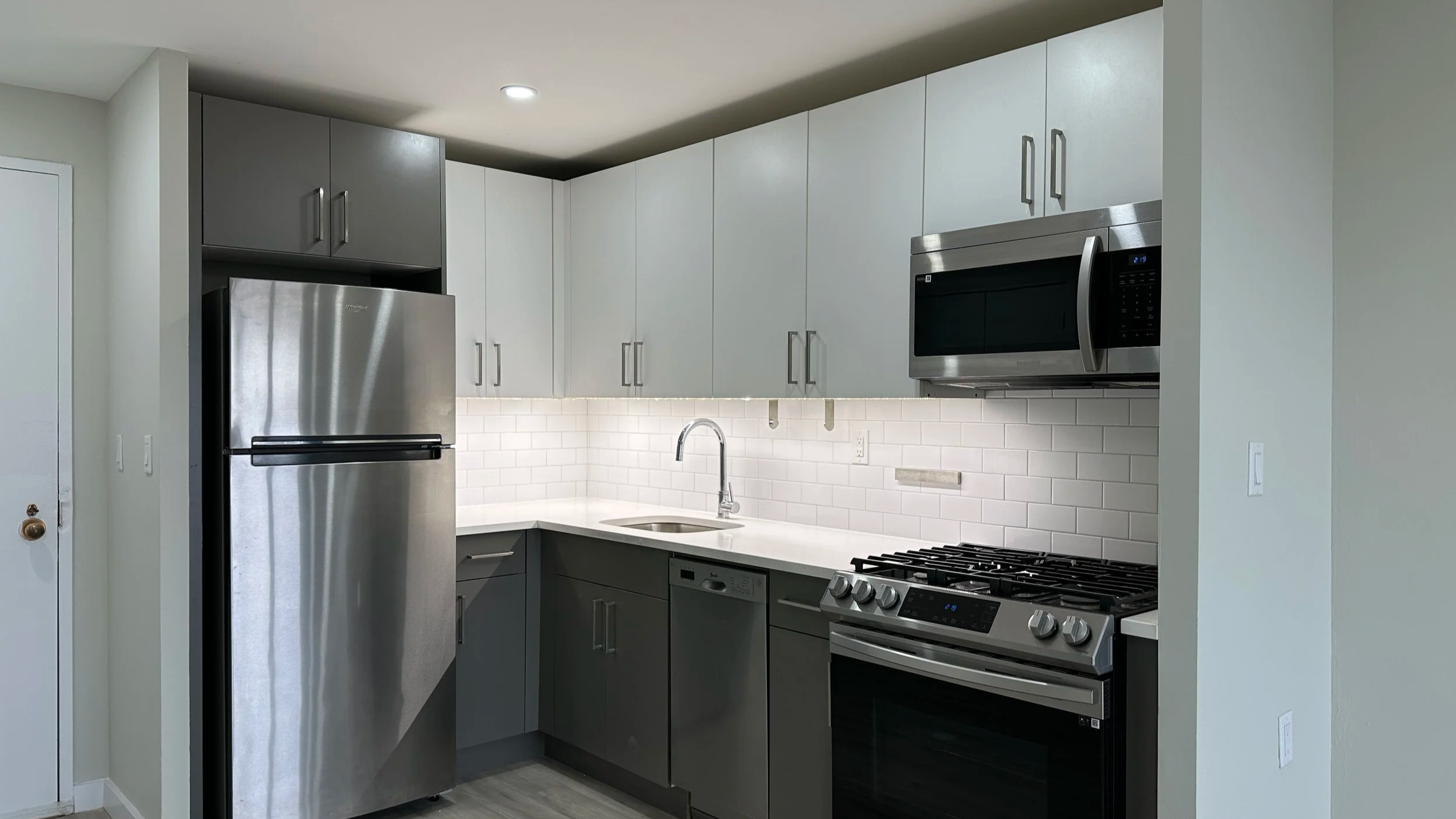 Modern kitchen with stainless steel refrigerator and oven, white subway tile backsplash, and gray and white cabinets.