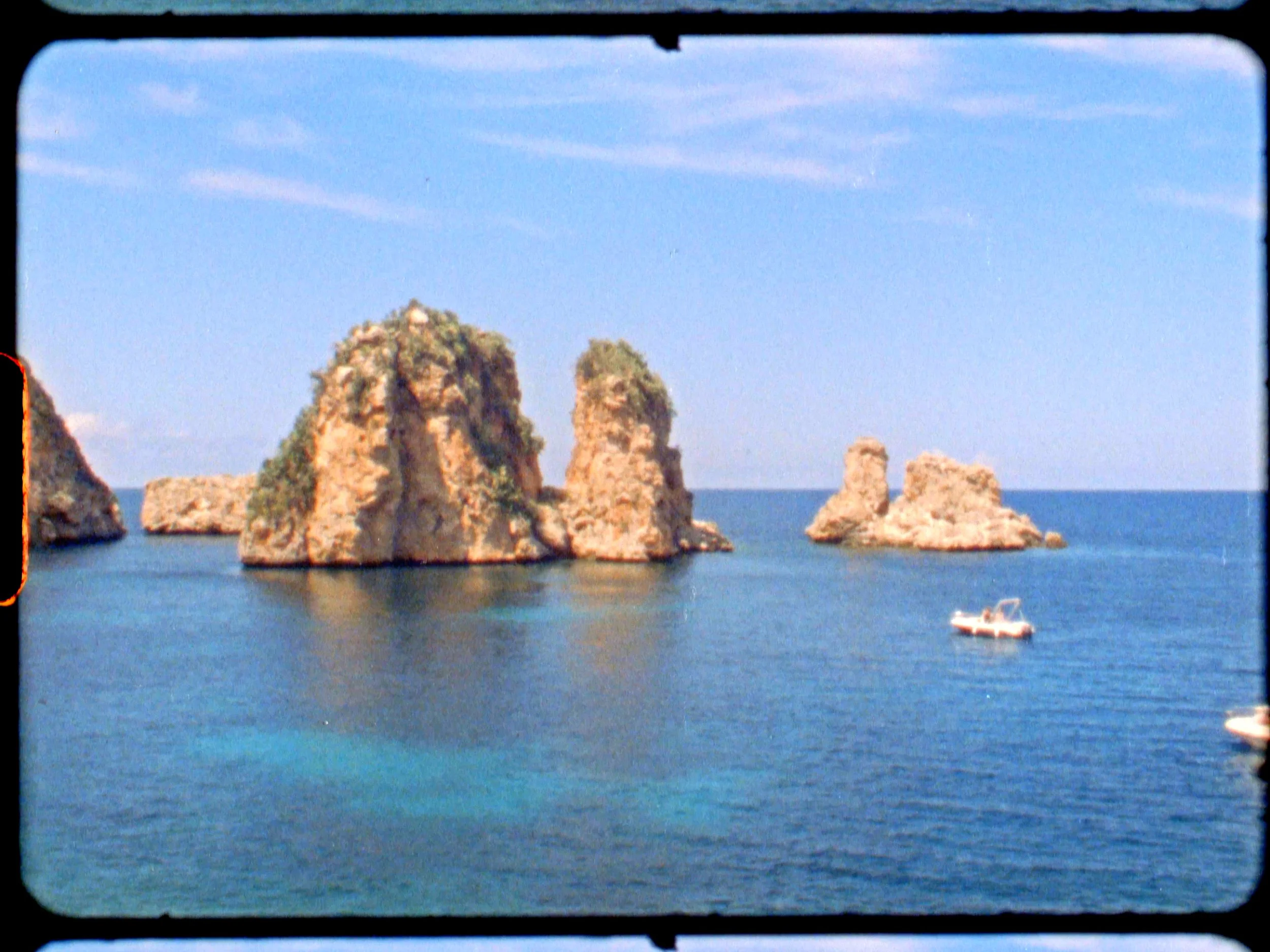 Sea stacks with greenery on top in ocean with a boat nearby, under a blue sky.