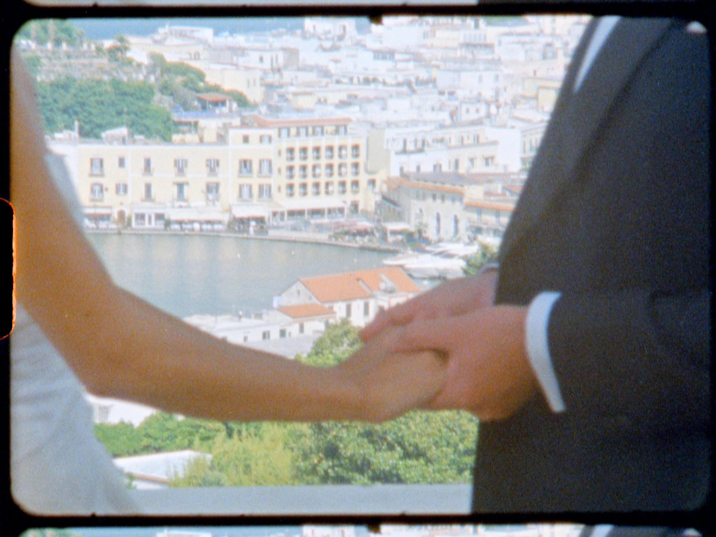 A couple holding hands in front of a cityscape with a body of water and various buildings.