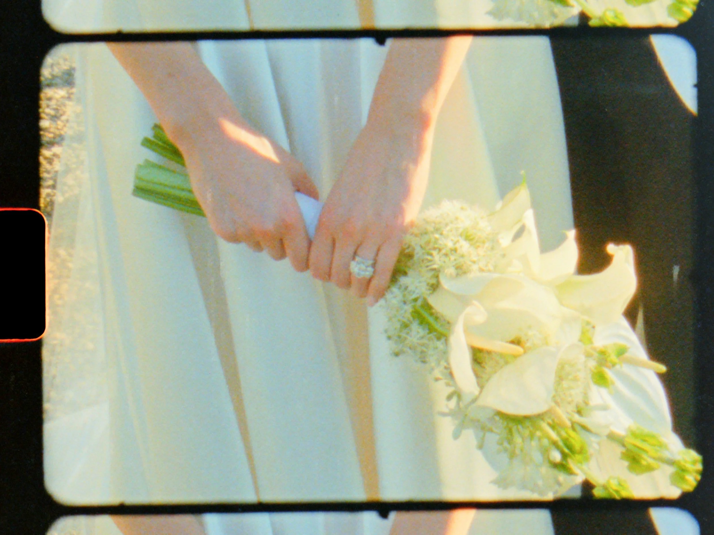 Close-up of hands holding a bouquet of white flowers, with one hand wearing a large diamond ring.