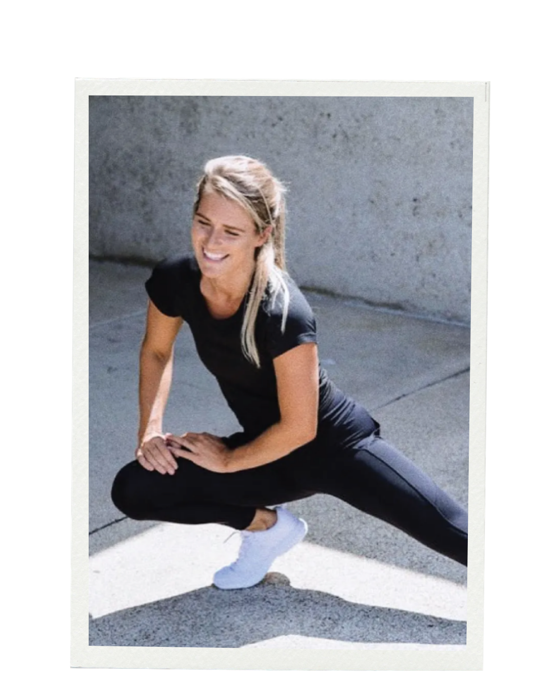 A woman in black athletic clothing performing a stretch outdoors on a concrete sidewalk near a gray wall, smiling. Alexz Hutsl. Branding & Websites Northern Rivers NSW