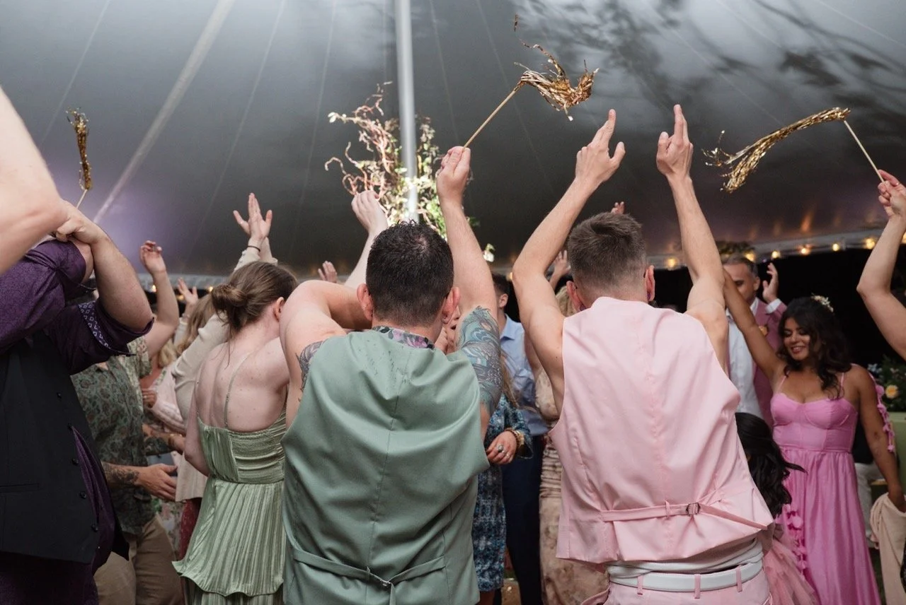 People dancing and celebrating under a tent, some holding gold party poppers.