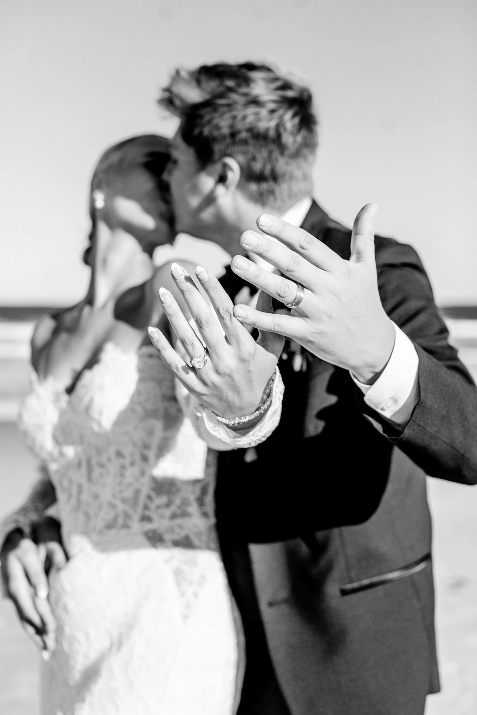A black-and-white photo of a couple kissing, holding hands, with the woman wearing a wedding dress and the man in a tuxedo.