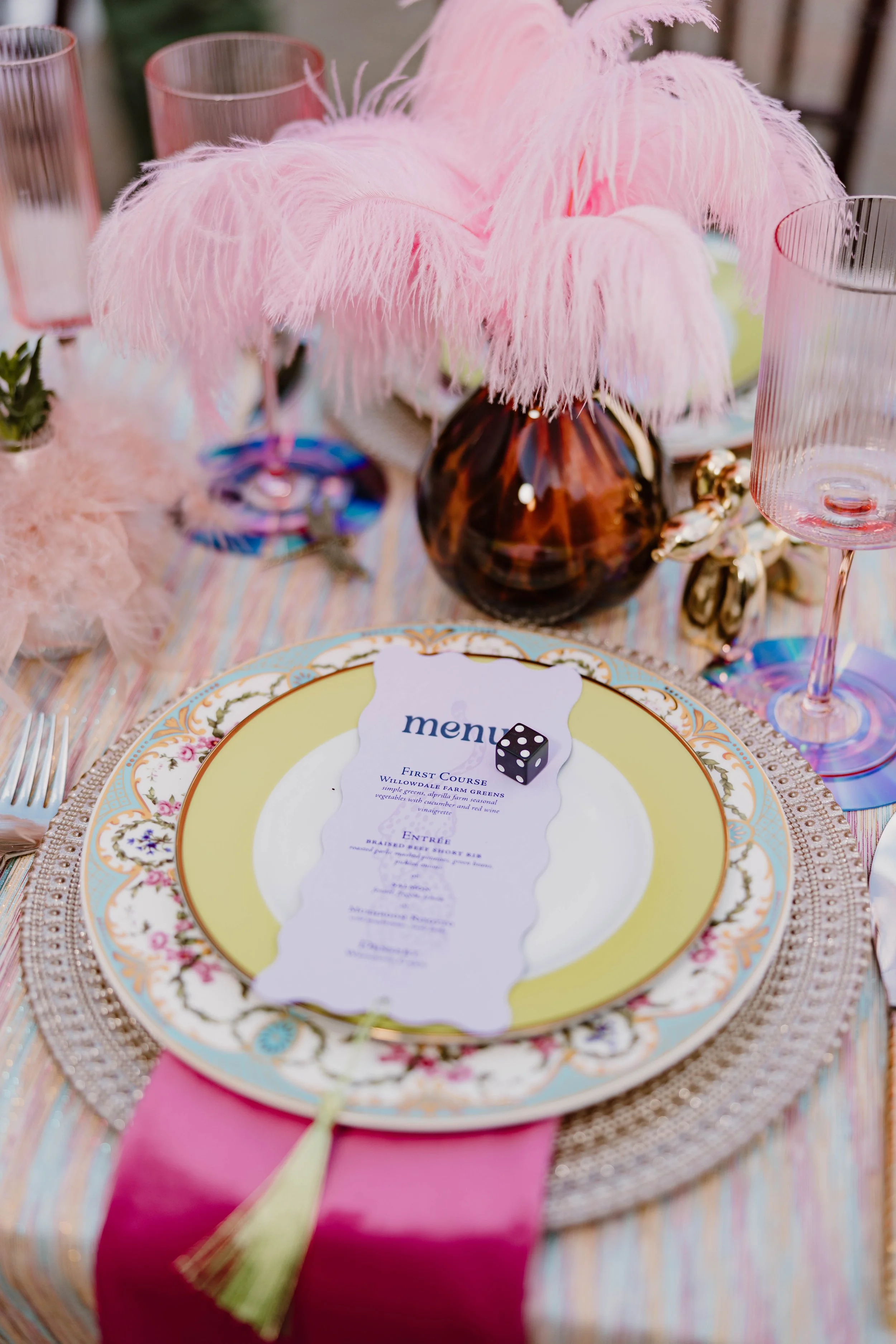 Decorative pink feather centerpiece on a formal dining table, with a menu, pink glassware, and a pink tablecloth.