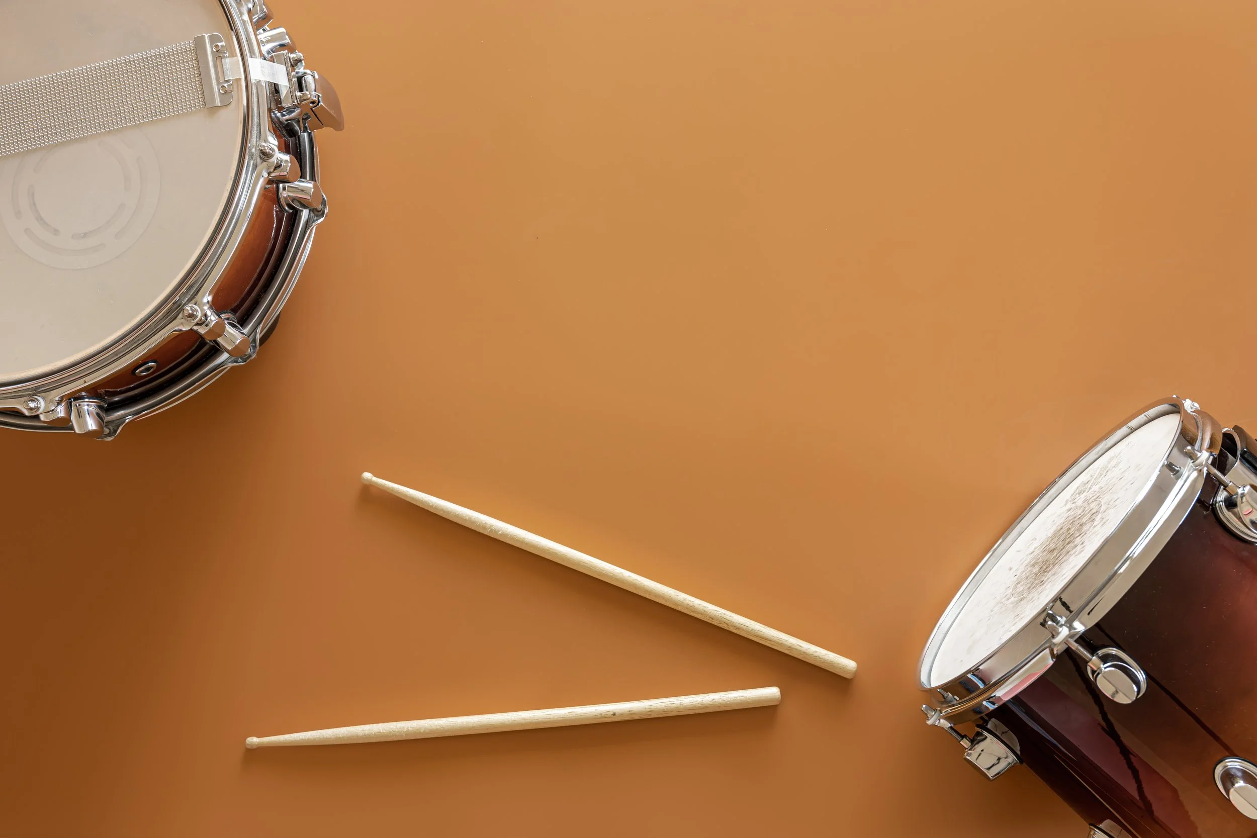 Tambores de percusión y baquetas sobre una superficie marrón.