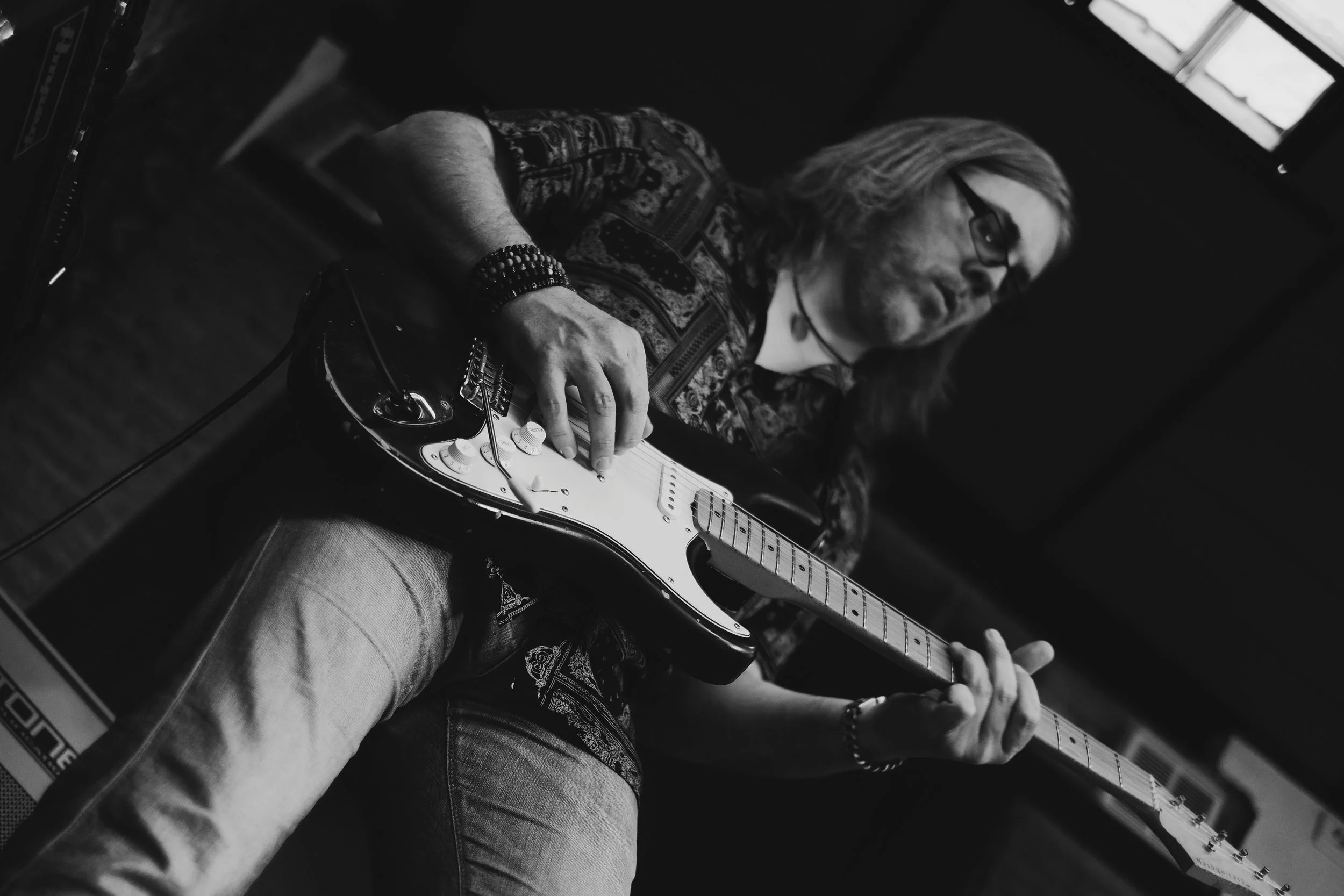 Persona tocando guitarra eléctrica en un entorno oscuro, en blanco y negro.